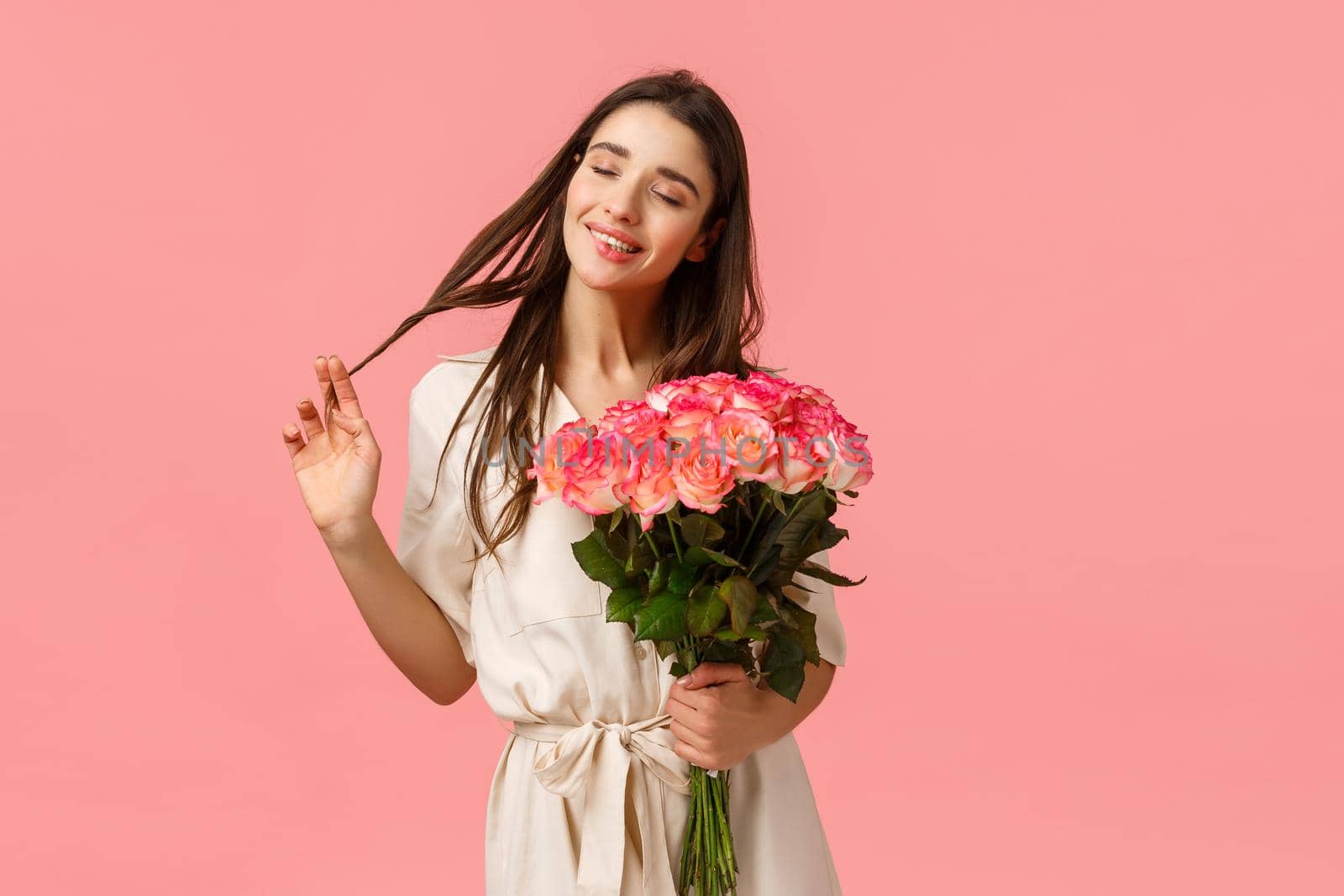 Tenderness, delight and valentines day concept. Charming, lovely and sensual brunette woman in dress, rolling curl on hair happily close eyes and dreaming, receive flower delivery, hold roses.