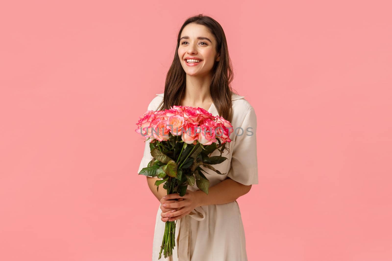 Valentines day, holidays, celebration and beauty concept. Charismatic attractive brunette female in dress, holding bouquet flowers, smiling delighted, receive present, standing pink background by Benzoix