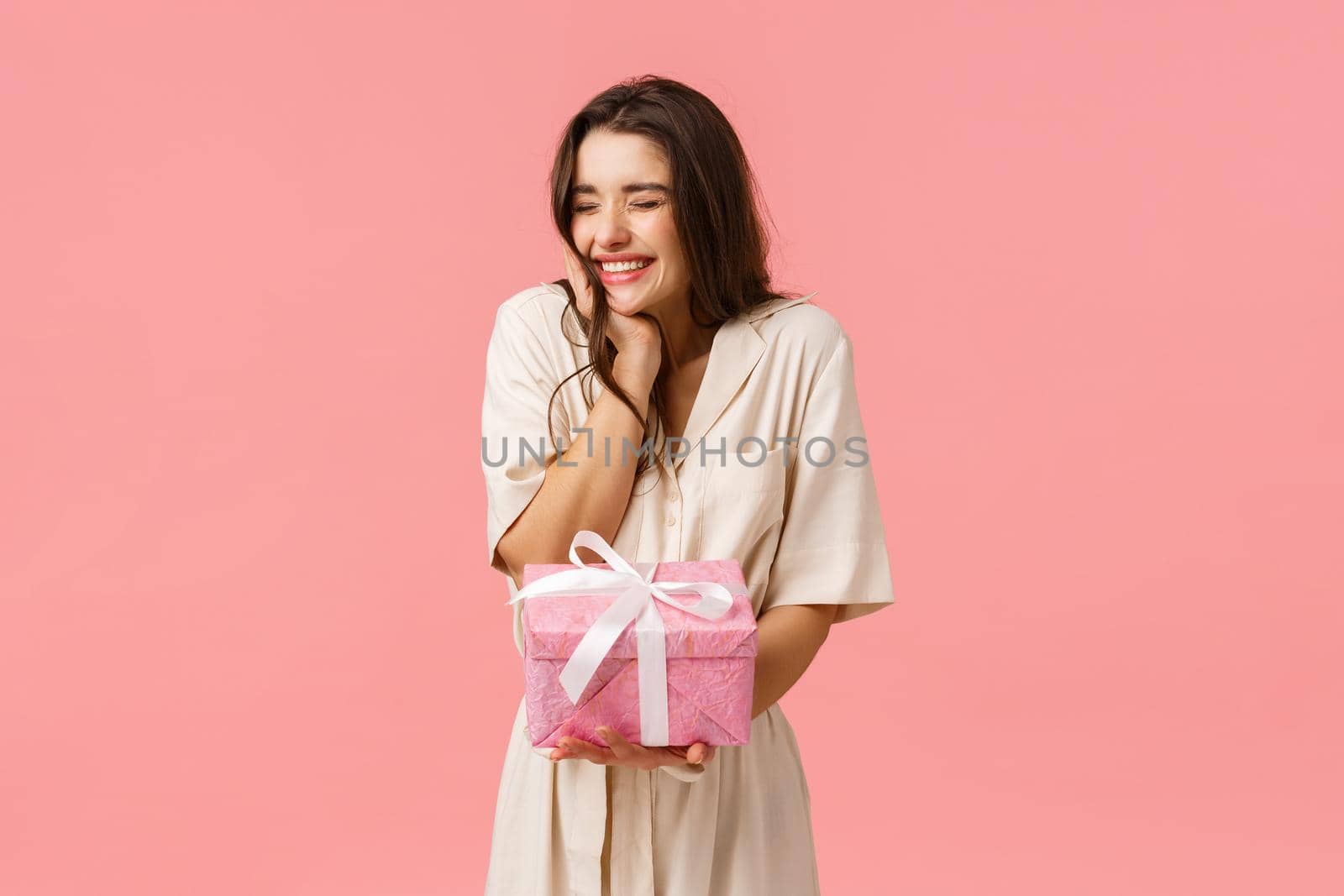 Anticipation, celebration and party concept. Cheerful lovely young woman in dress, cheering close eyes happily smiling and laughing, receiving nice present, got pretty gift, pink background.