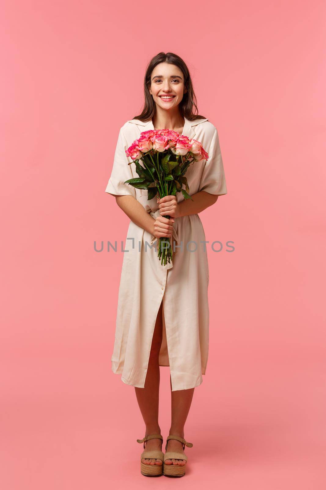 Full-length vertical portrait attractive, lovely young woman receiving beautiful flowers, holding bouquet enjoying romantic date, smiling happily, standing pink background delighted by Benzoix