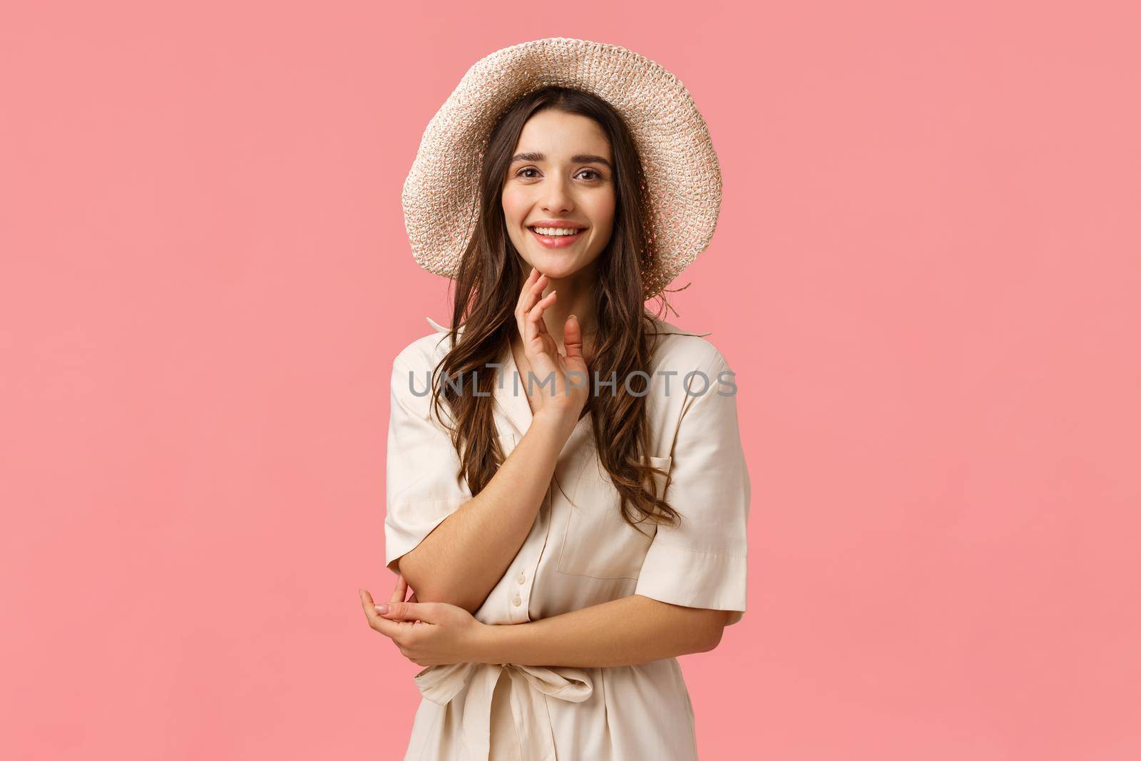 Vacation, beauty and shopping concept. Cheerful tender glamour brunette female in dress, fancy hat, standing elegant and cute over pink background, smiling having casual conversation by Benzoix