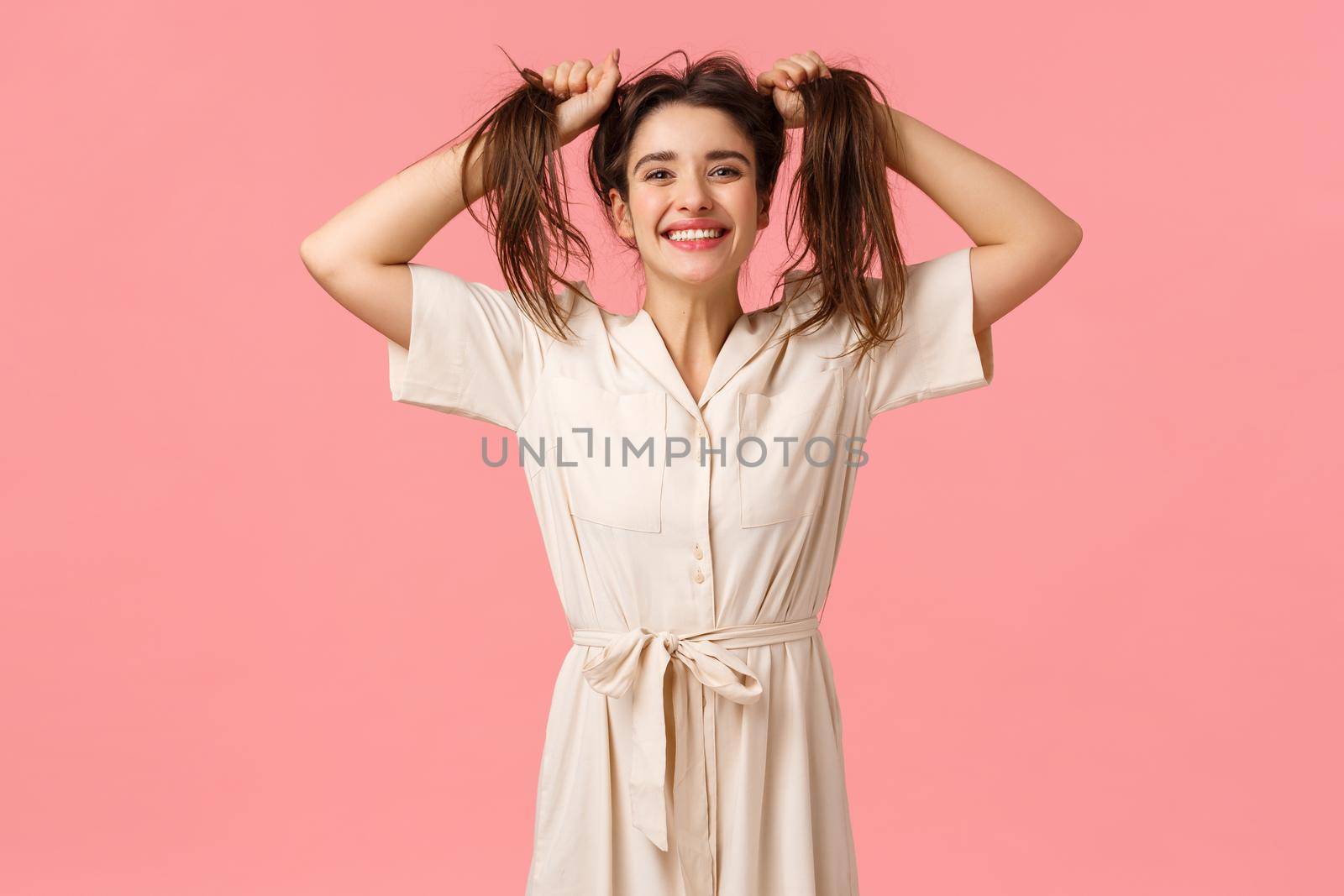 Joy, party and happiness concept. Silly funny girl having fun fooling around, pulling hair sideways making it messy, smiling cheerfull, enjoy perfect day feeling amused and upbeat, pink background.