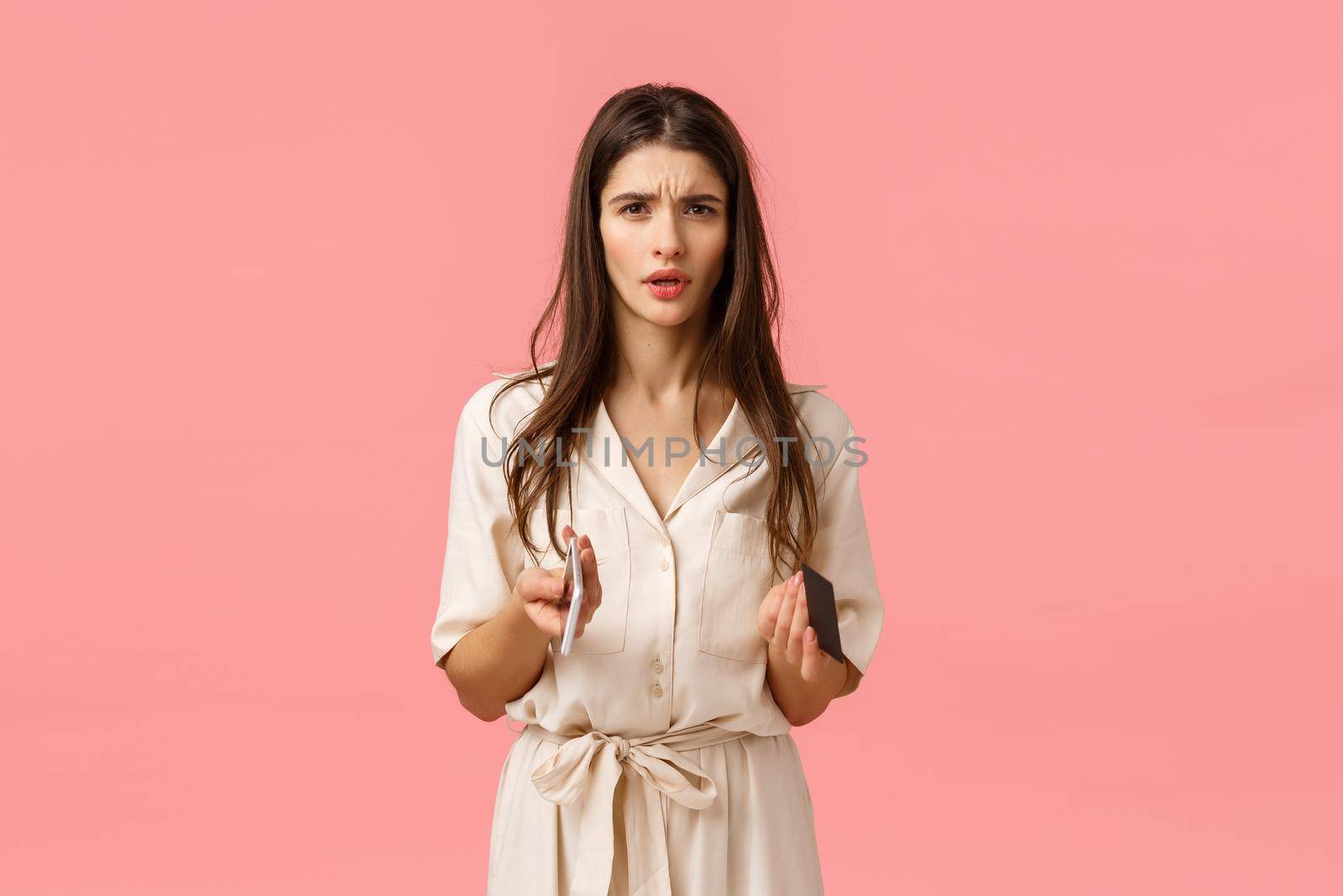 Finance, technology concept. Troubled and worried young frustrated woman cant understand what happened, frowning looking perplexed and cocnerned, holding credit card with smartphone, pink background by Benzoix