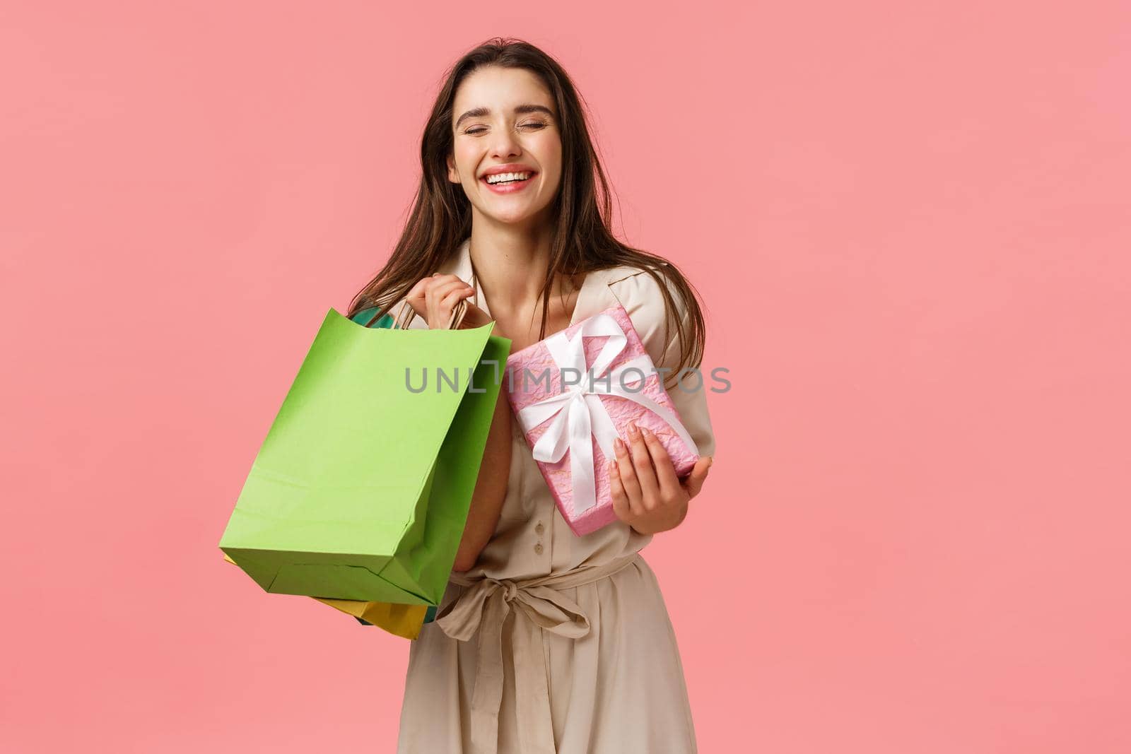 Happiness, presents and celebration concept. Cheerful happy and carefree b-day girl enjoying shopping, have a nice day store, holdin shop bags and gifts, close eyes laughing excited, pink background.