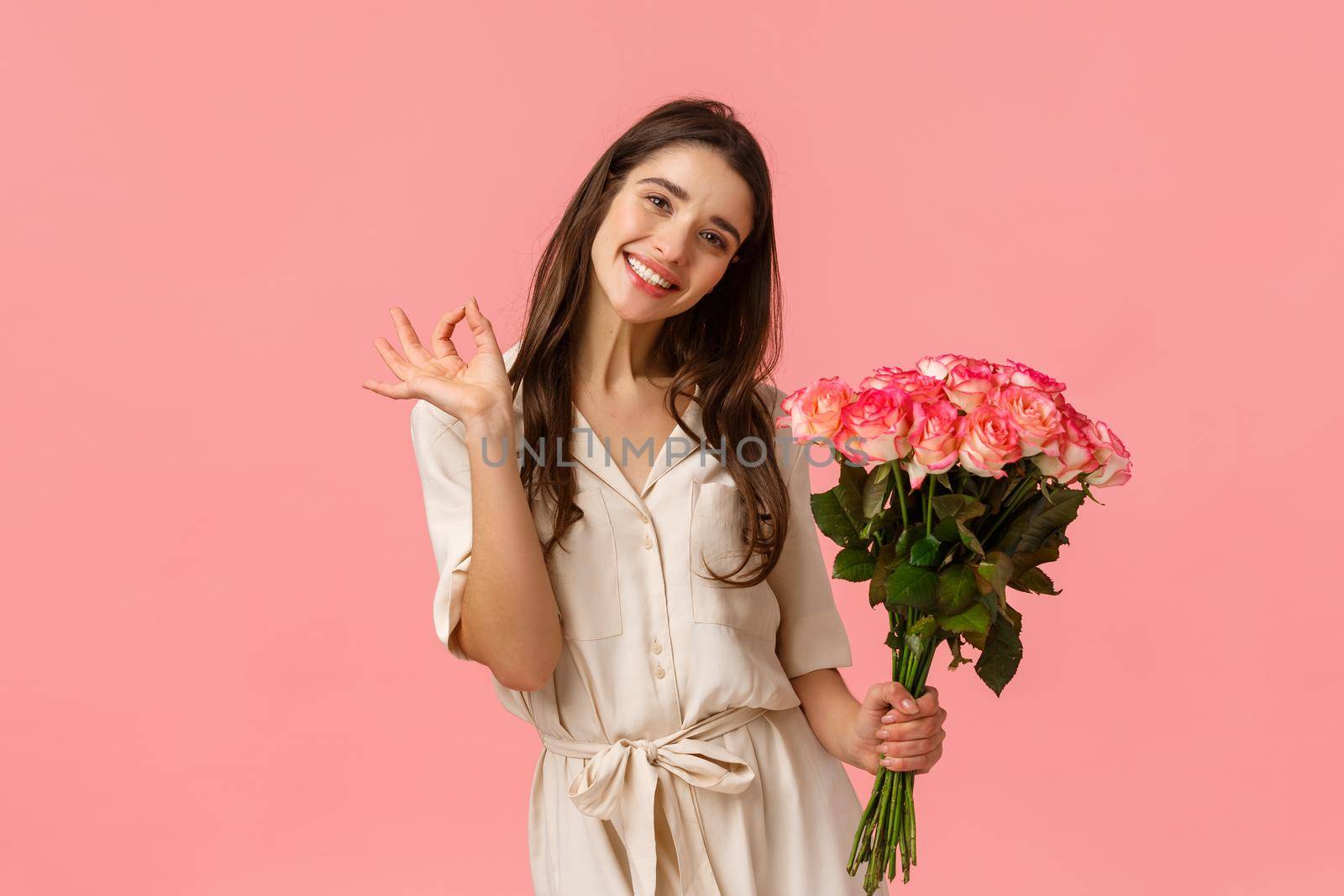 Lovely, dreamy and coquettish brunette female in dress, tilt head and smiling delighted, showing okay, good holding roses, got gift on valentines day, beautiful bouquet flowers, pink background by Benzoix