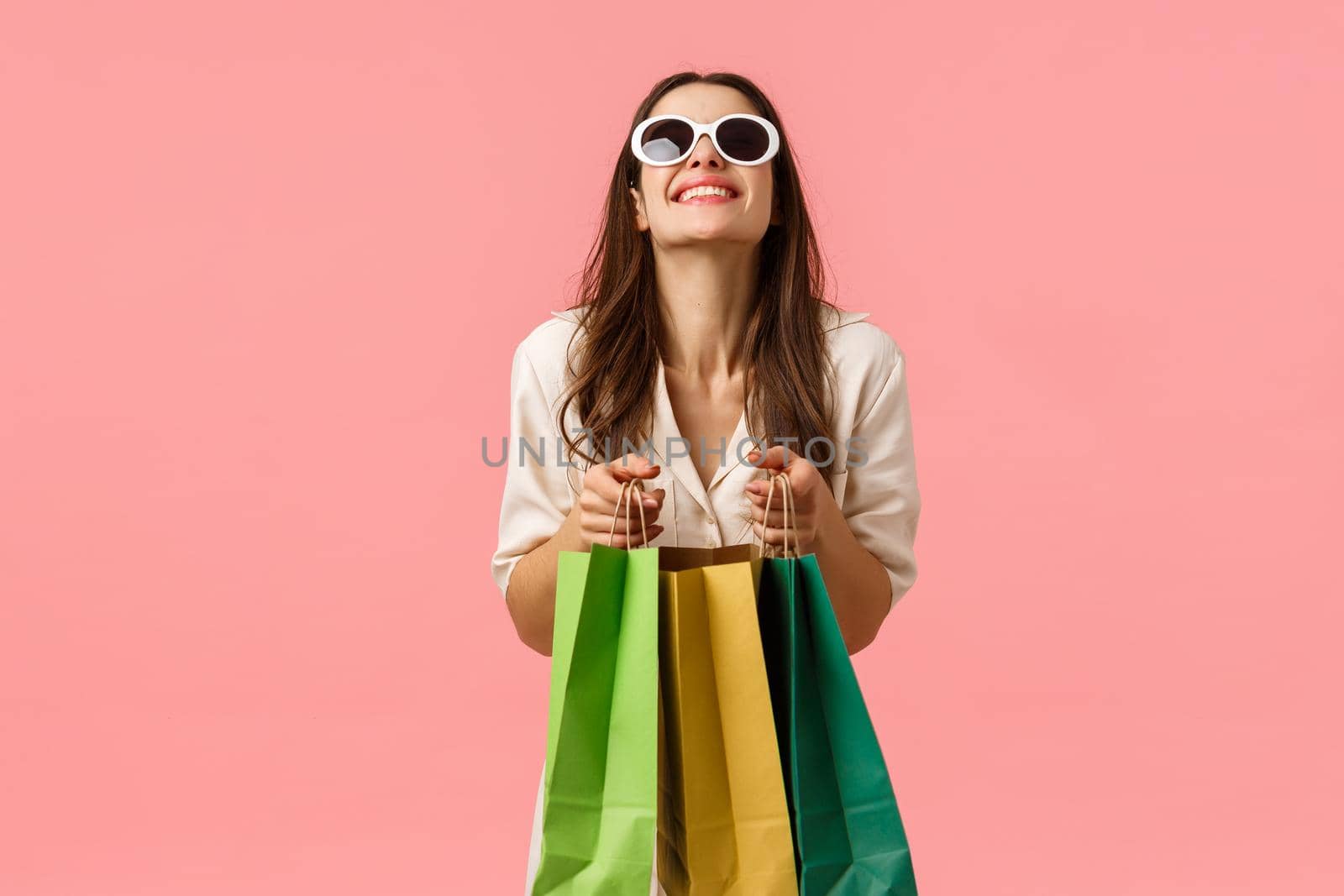 Shopping, fashion and beauty concept. Happy and excited girl buying new clothes for summer vacation, packing up, holding shopping bags, laughing standing pink background enthusiastic.