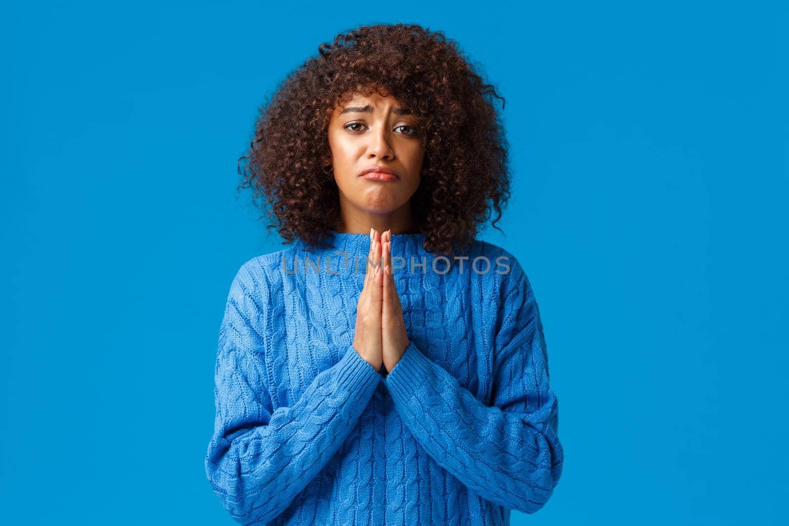 Please help me. Sulking gloomy cute african-american female friend with afro haircut, press hands together in pray, supplicating, asking apology, sorry for mistake, begging over blue background by Benzoix