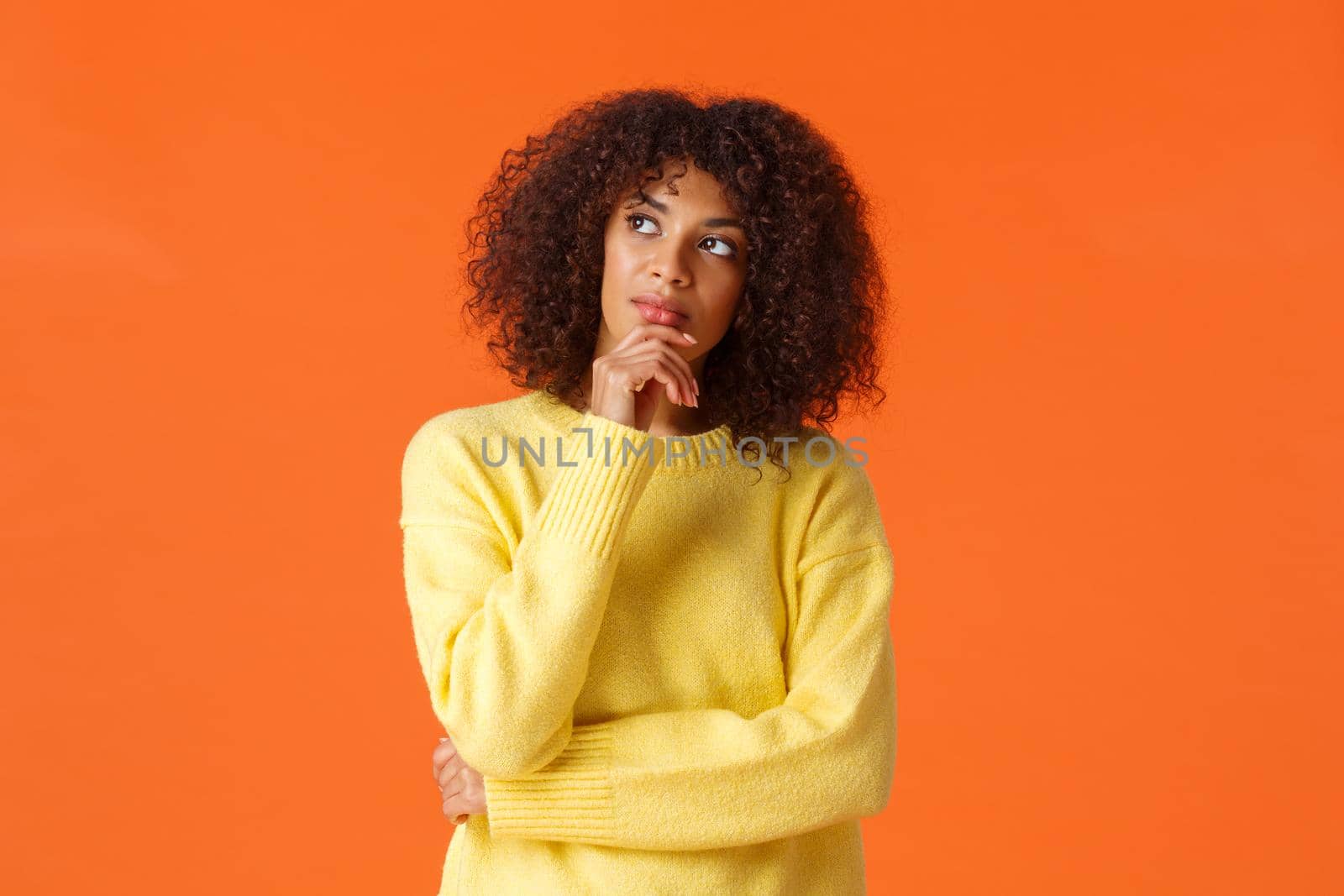 Waist-up portrait unsure, thoughtful young creative african-american female entrepreneur making new ideas, standing orange background, searching inspiration, thinking looking up.