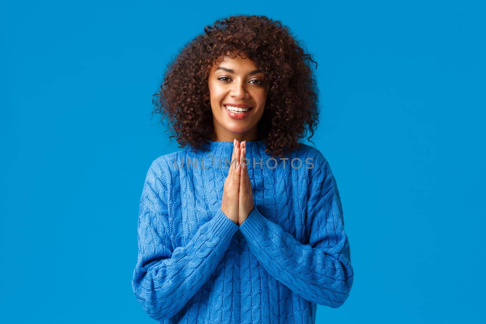 Thankful cute smiling african-american pretty woman with afro haircut, saying arigato and smiling, clasp hands together near chest looking grateful, showing respect, standing blue background by Benzoix