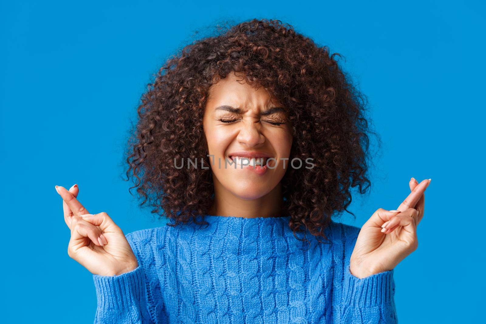 Putting all efforts in pray for wish come true. Hopeful cute african-american woman desire dream fulfill, close eyes and smiling eager win, cross fingers good luck, praying, blue background by Benzoix