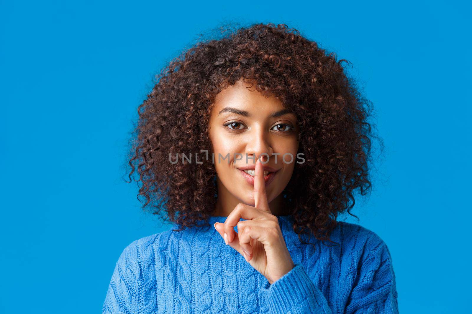 Close-up portrait sensual and mysterious african-american woman with cute happy smile, shushing, press index finger to lips having secret, prepare surprise and hush looking camera, blue background by Benzoix