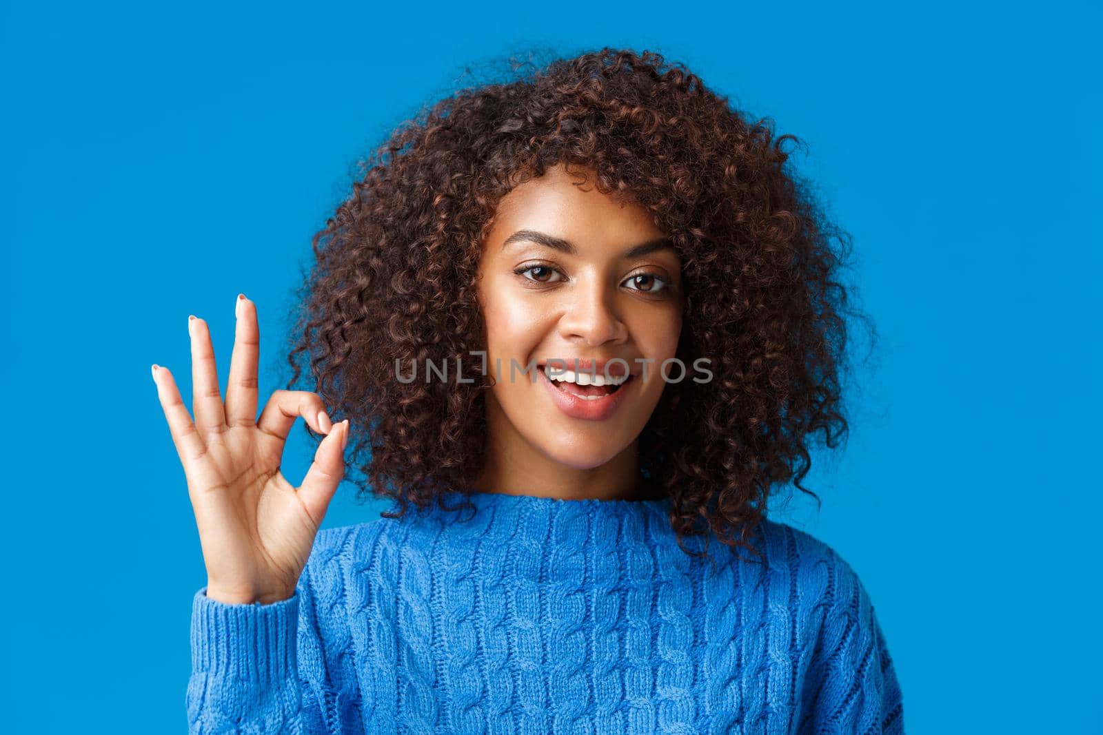 Alright, all great. Satisfied good-looking african-american female customer, rate good service, give positive feedback, showing okay, ok excellent gesture and smiling in approval, blue background.