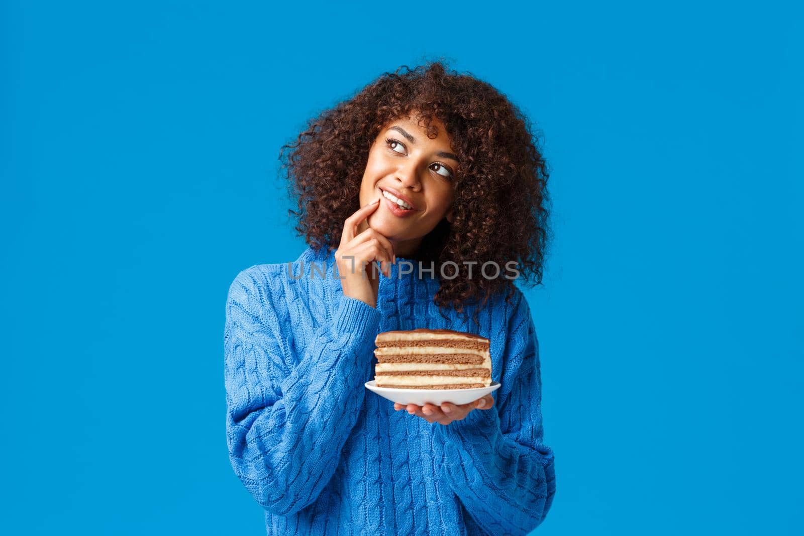 Dreamy and silly thoughtful african american girlfriend prepared cake as present for boyfriend on valentines day, standing over blue background look up smiling imaging something cute, blue background.