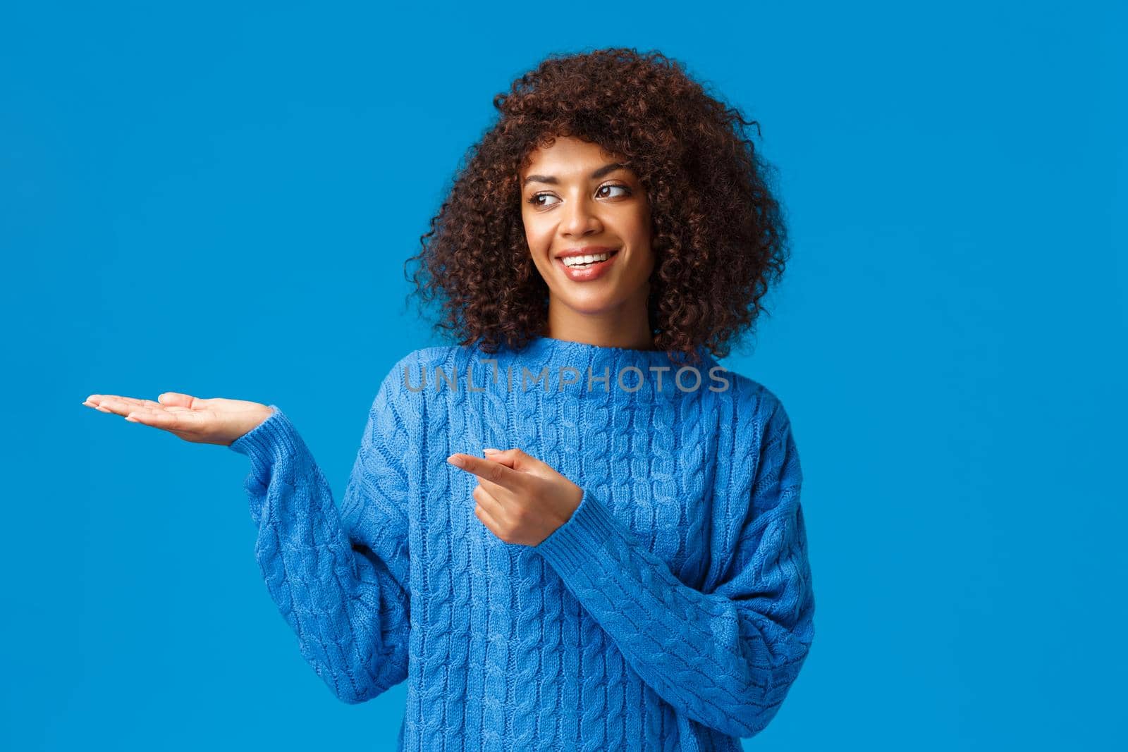 Charismatic lovely smiling african-american female helping family arrange table for holidays gathering, pointing finger left, presenting something on hand, standing blue background joyful by Benzoix