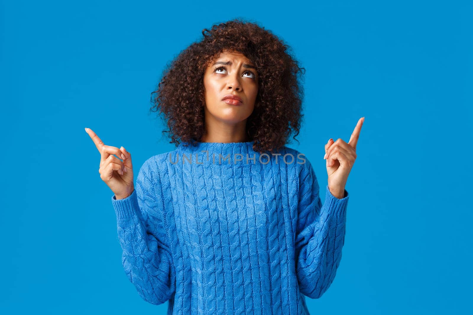 Skeptical and upset, gloomy timid african-american woman dont like whats happening, express disapproval and sadness, looking pointing up jealous, envy of friend bought she wanted, blue background by Benzoix