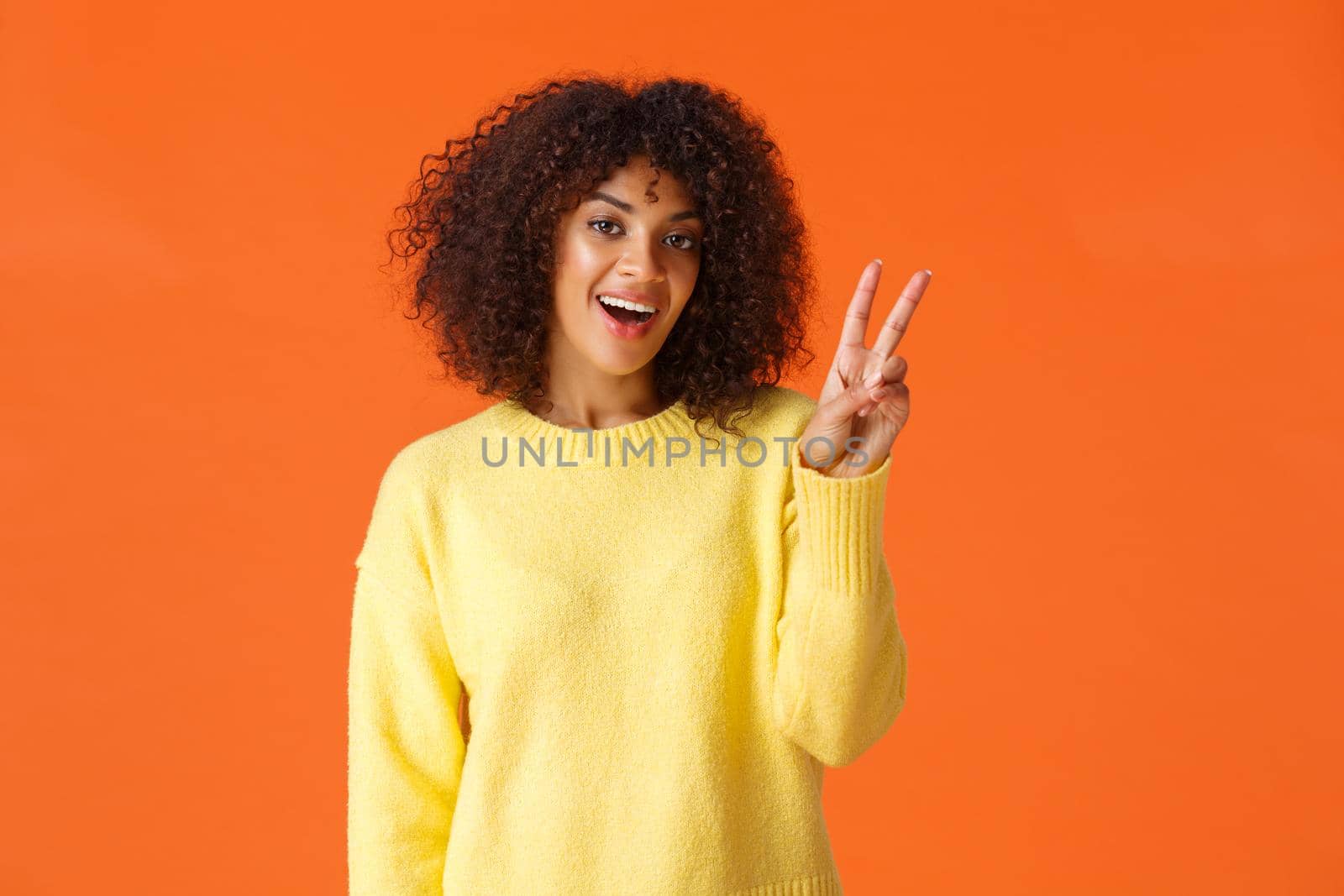 Carefree lovely, silly african-american girl posing for photo over orange background with smile, showing peace sign saying cheese feeling joyful and upbeat, express positive emotions by Benzoix