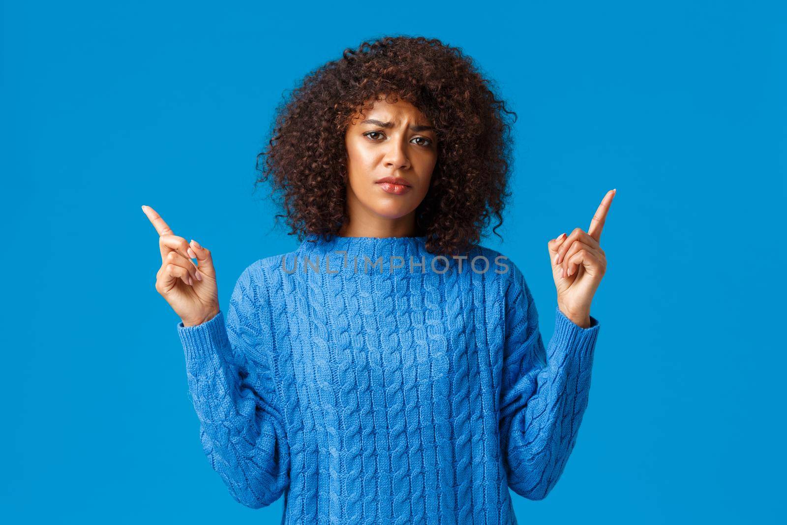 Girl talking about bad experience feeling uneasy and upset. Grimacing cute gloomy african-american woman with afro haircut, frowning indecisive and displeased, pointing fingers up.
