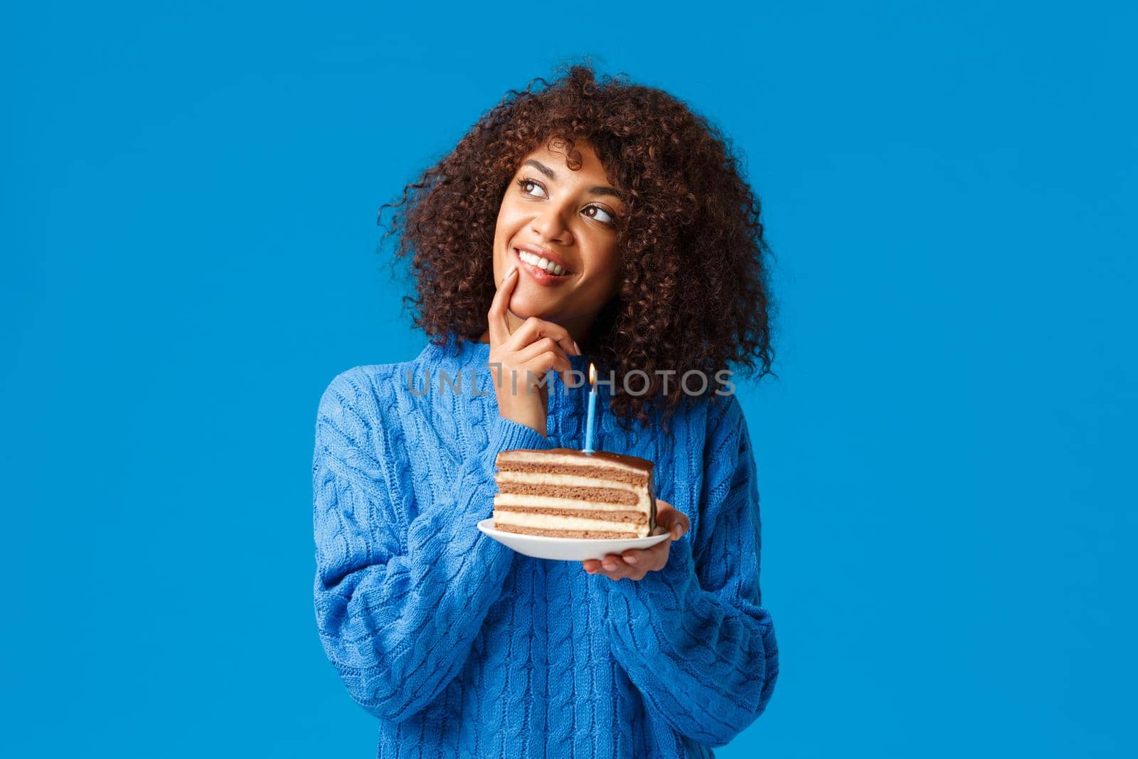 Dreamy and happy, beautiful african-american woman with afro haircut, thoughtful gazing up, smiling and touch lip as thinking what wish for before blowing-out candle in birthday cake by Benzoix