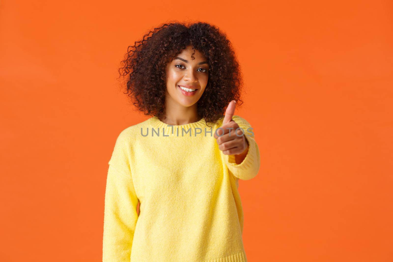 Waist-up portrait cheerful satisfied girl made her final choice, showing thumb-up in approval or like, recommend product, nod agreement, smiling delighted, standing orange background.