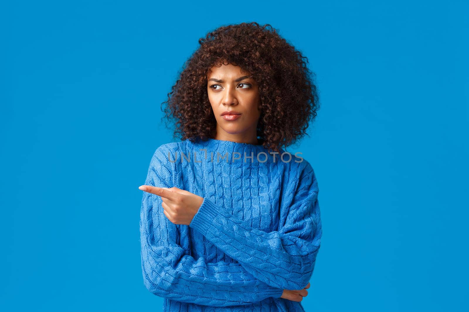 What a heck. Displeased and reluctant african-american bothered woman with afro haircut, pointing looking left with disapproval, express condemn or scorn, standing unsatisfied blue background.