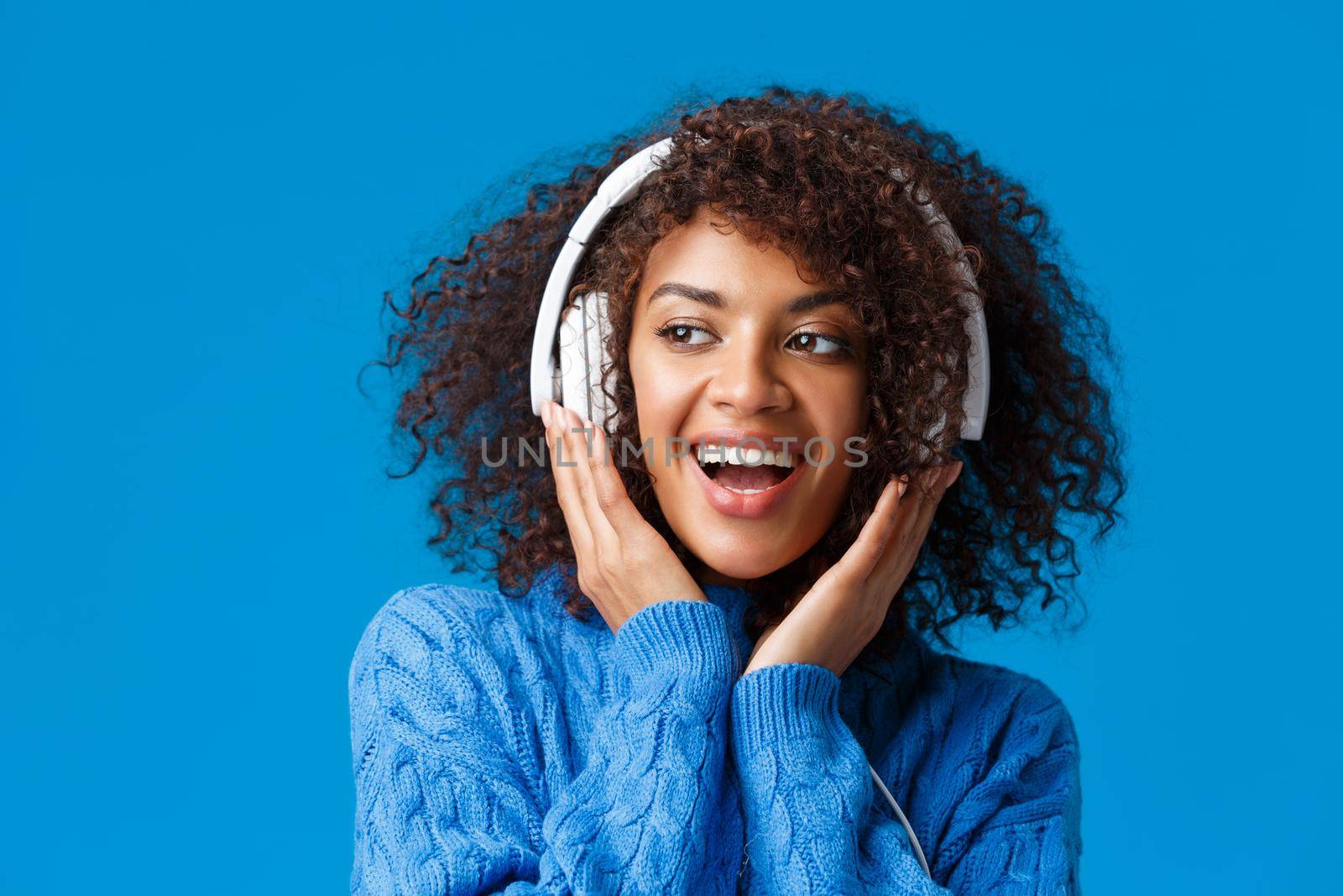 Close-up portrait cheeky and carefree happy smiling african-american modern gen-z girl with afro haircut, curly hair, listen music in headphones smiling delighted, enjoy new earphones by Benzoix