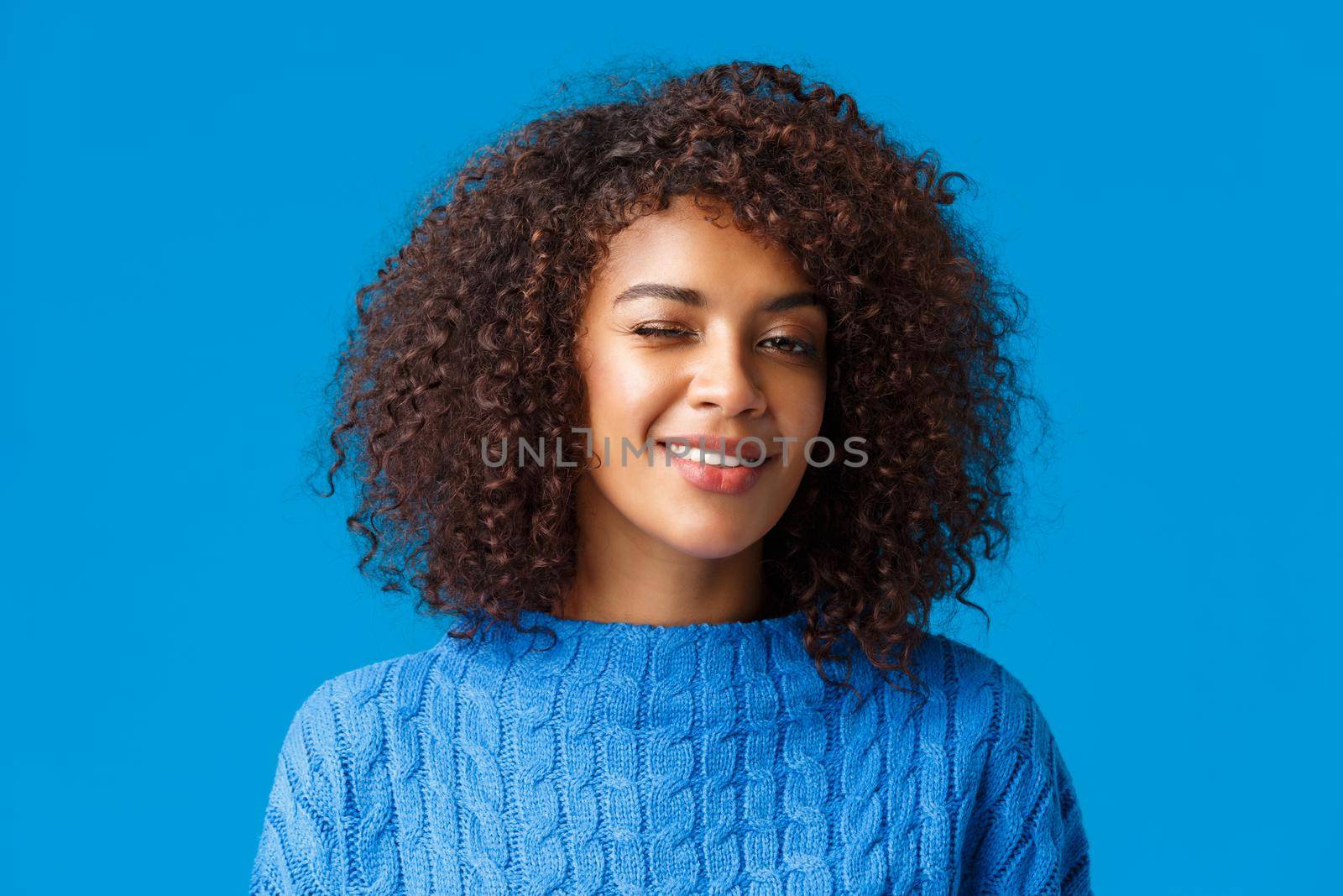 Everything be alright, relax and enjoy holidays. Cheerful cute and coquettish african american hipster girl with afro haircut, winking encourage all good, smiling, blue background.