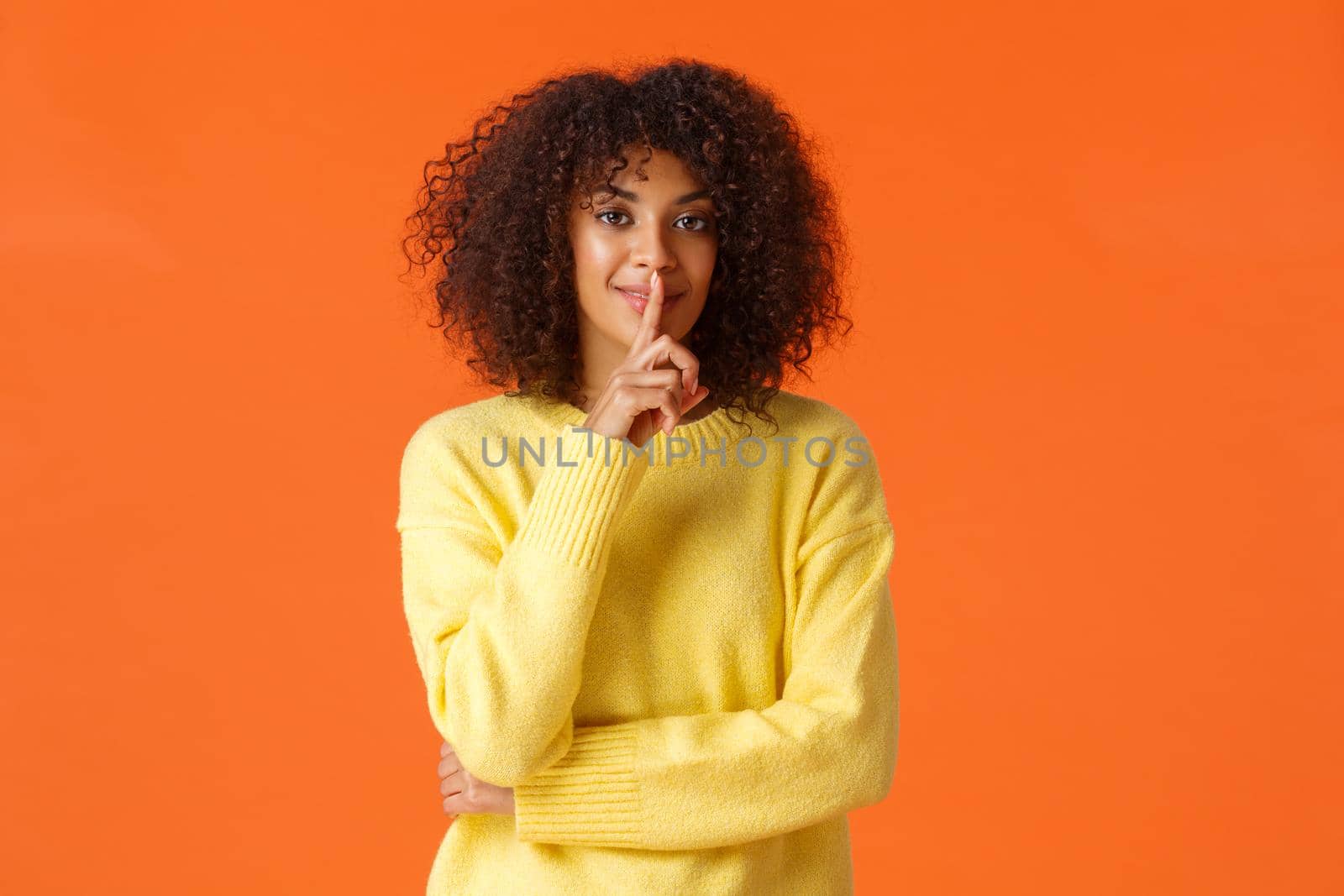 Waist-up shot sensual african-american woman have secret plan, ideas for holiday gifts, shushing, press index finger to lips silence, quiet gesture, smiling prepare surprise, orange background.