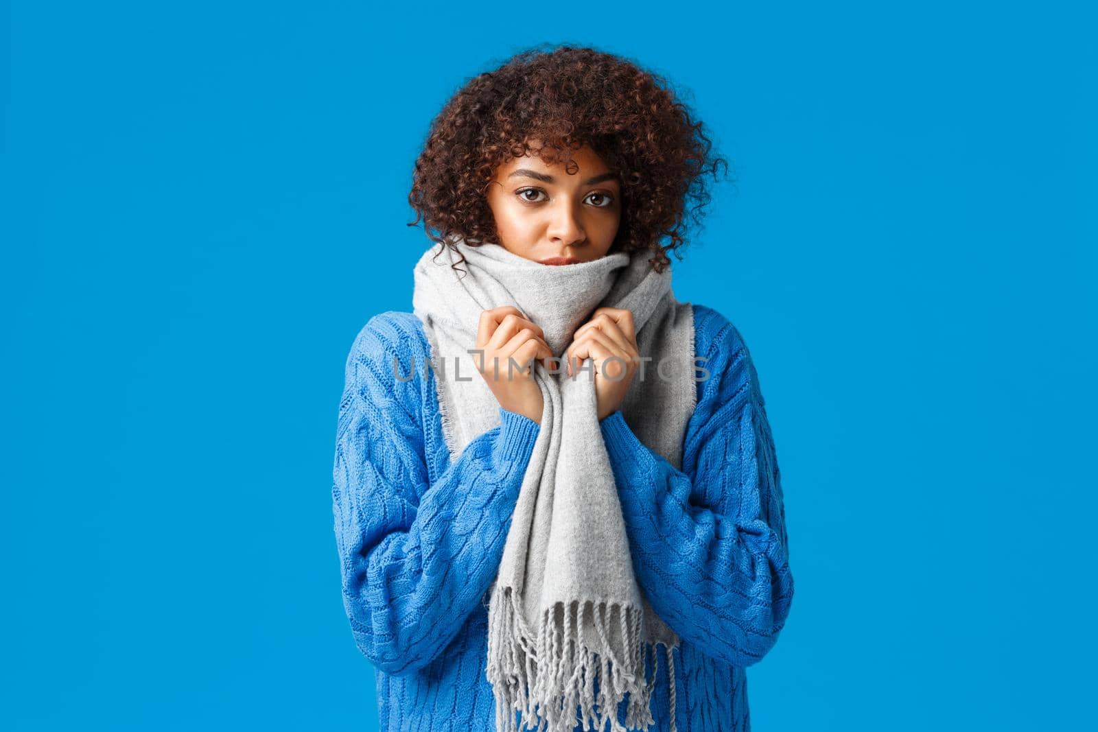 Cute and gloomy young african-american lovely woman with afro haircut, wrap herself with warm scarf, feeling chilly or cold in winter, standing blue background, waiting someone fix heater.