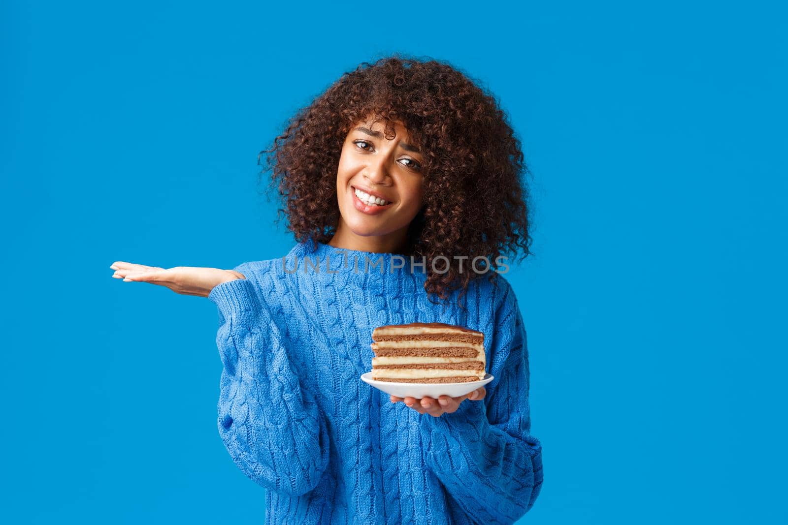 Unsure and clueless attractive african-american female in sweater, shrugging look uncertain, dont know eat or no, holding plate with tasty cake full calories, standing blue background.