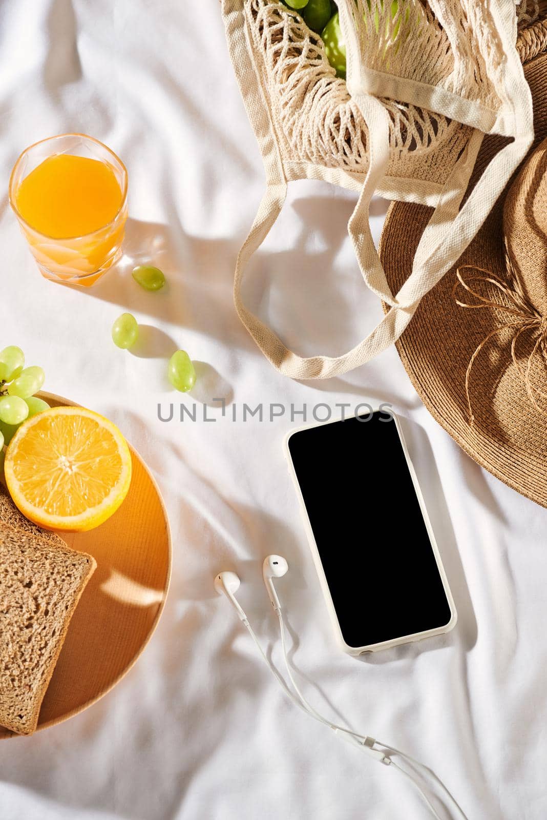 Picnic background with bag, bread and straw hat, glasses, orange juice, phone on white background.