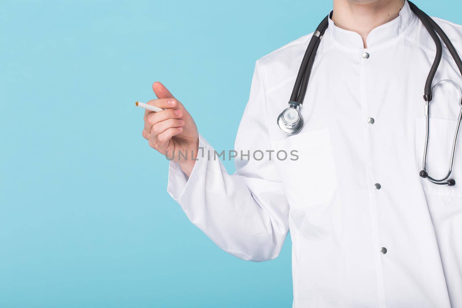 Stressed doctor smoking cigarettes on blue background.