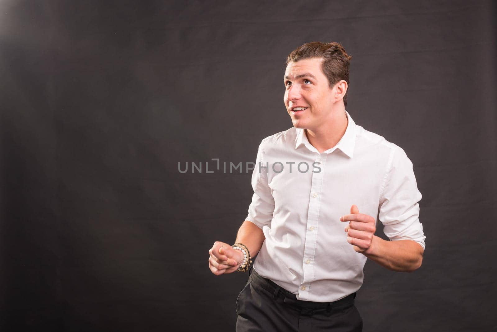 Dancing, happiness, people concept - handsome man in white shirt dancing over the grey background with copy space.