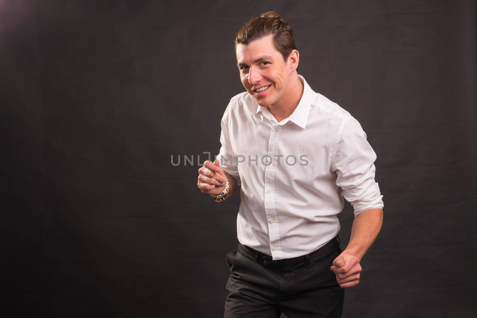 Dancing, happiness, people concept - handsome man in white shirt dancing over the grey background with copy space.