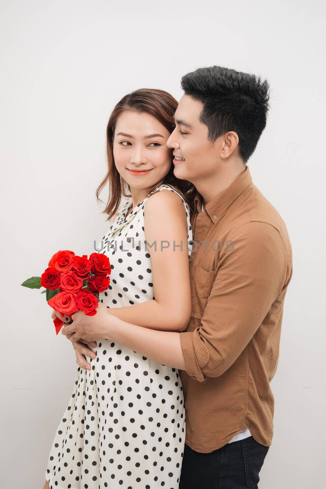 Beautiful young woman hugging her boyfriend and holding nice bouquet of red roses