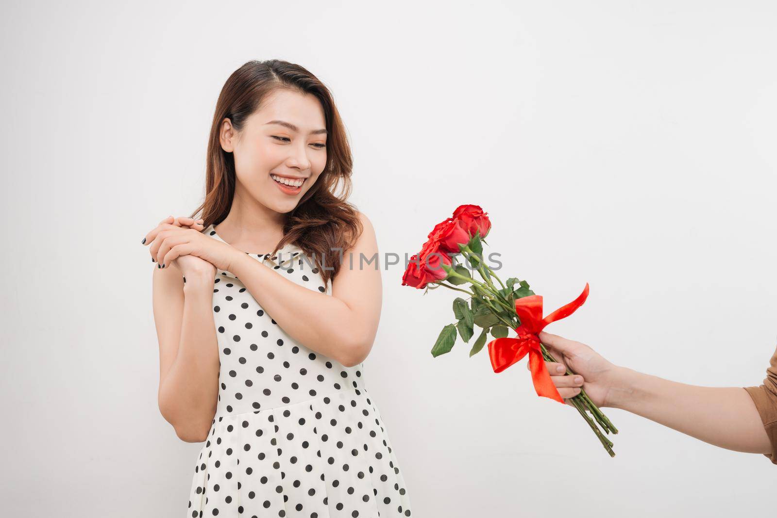 Cheerful charming young woman receiving bunch of flowers from her boyfriend over white background