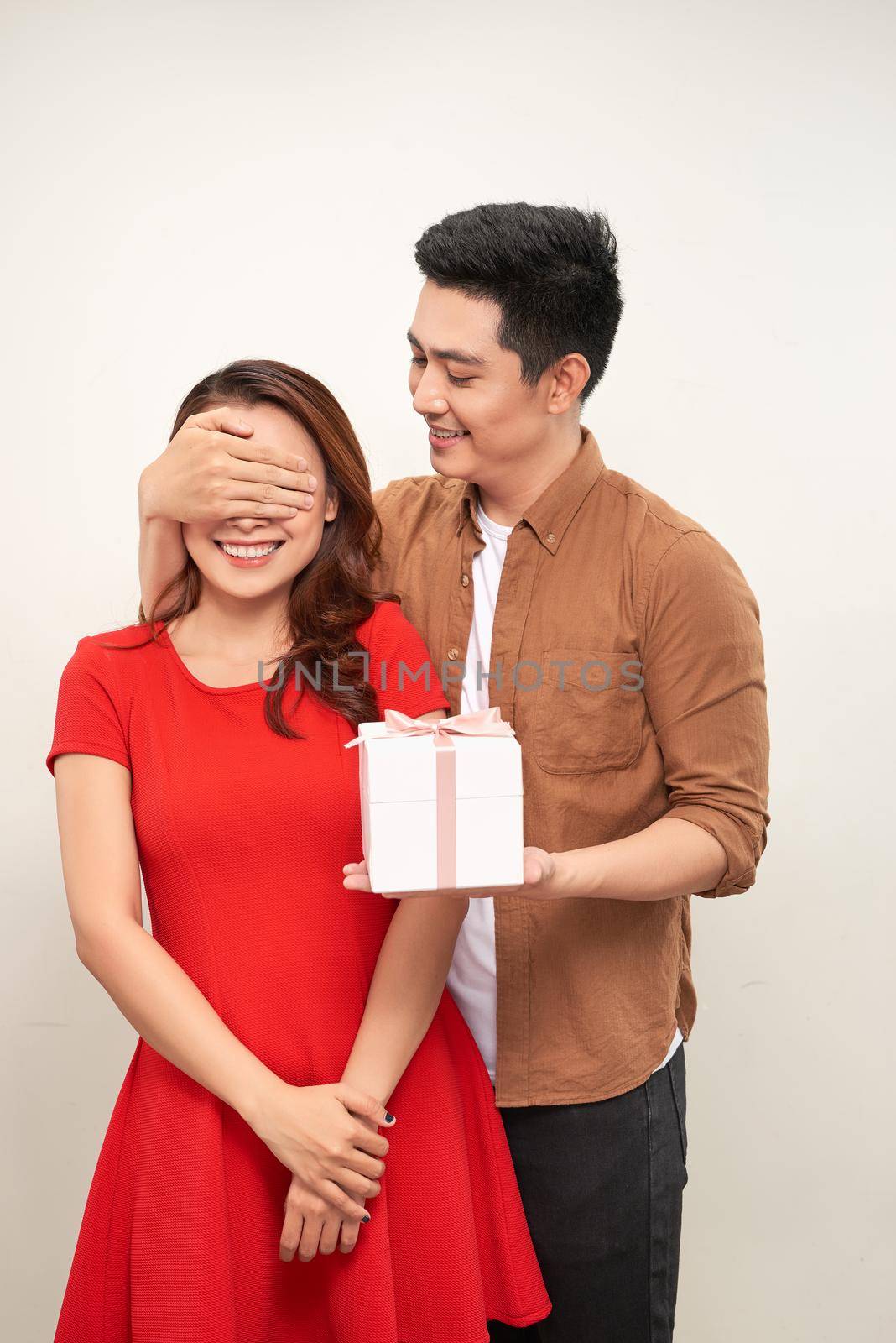 Portrait of a happy young couple standing over white background, holding gift boxe, cover eyes by makidotvn