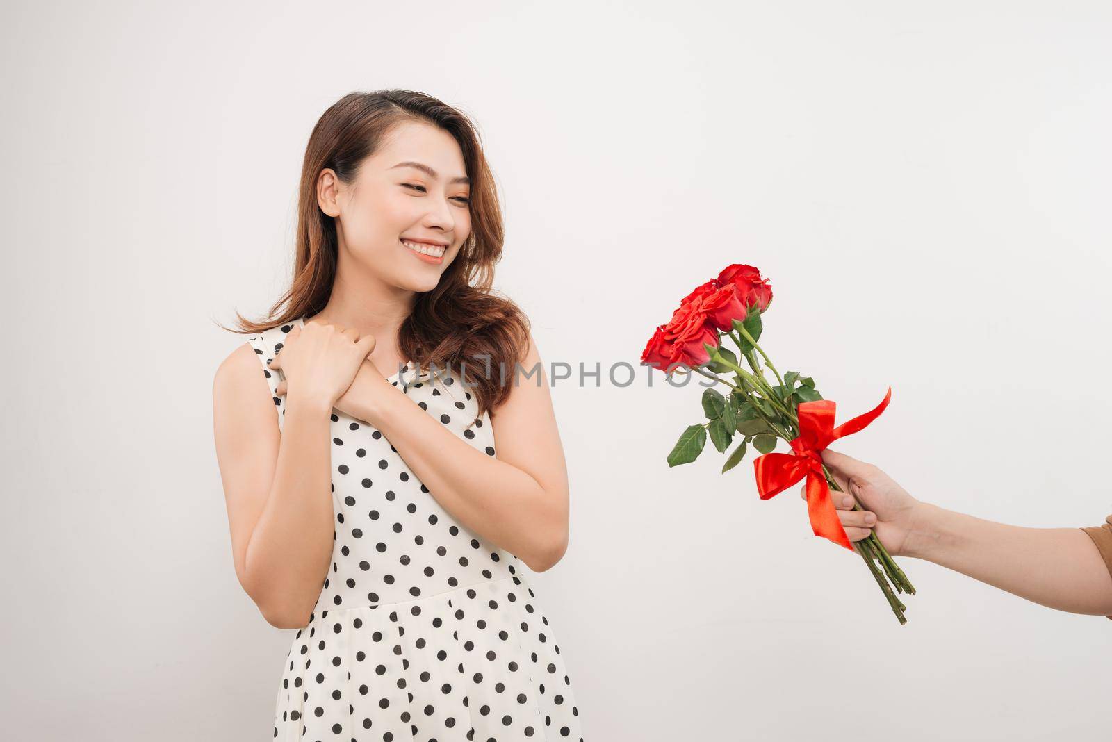 Cheerful charming young woman receiving bunch of flowers from her boyfriend over white background