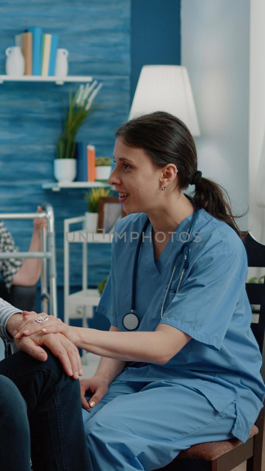 Nurse giving assistance to retired man with disability in nursing home. Invalid patient sitting in wheelchair, receiving support and help at healthcare checkup visit. Disabled person