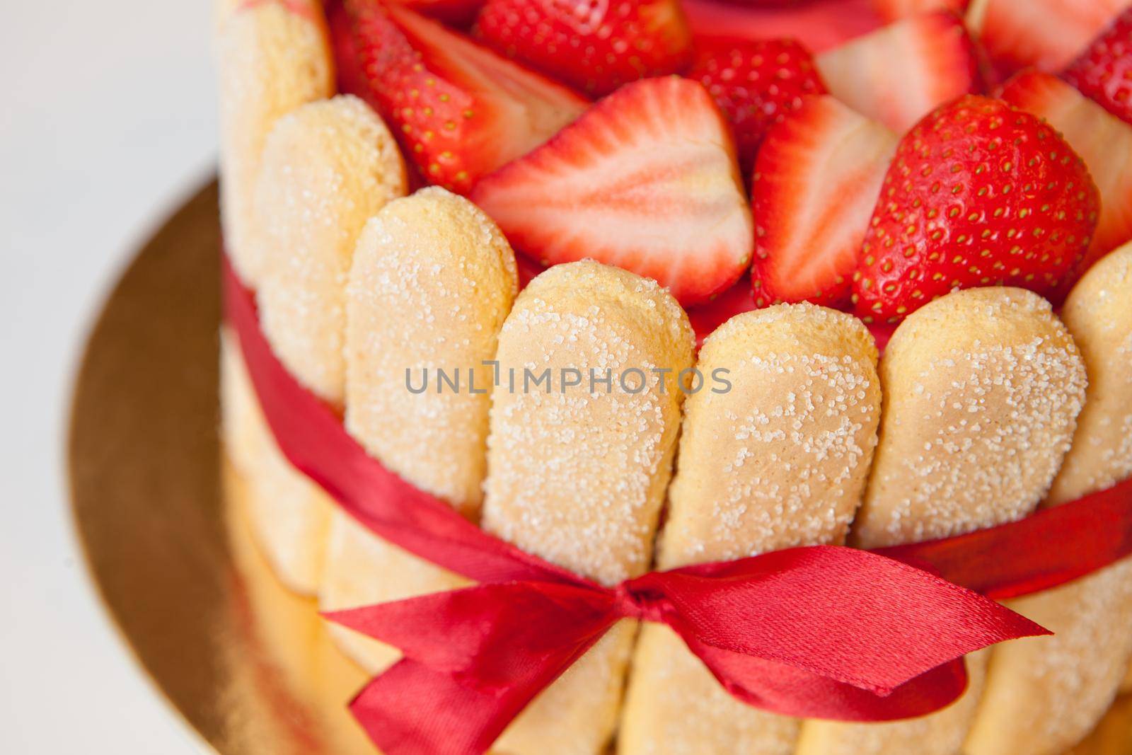 tiramisu cake close up with strawberries, ladyfingers, mascarpone and red bow-tape isolated on white. summer fruit charlotte cake on table