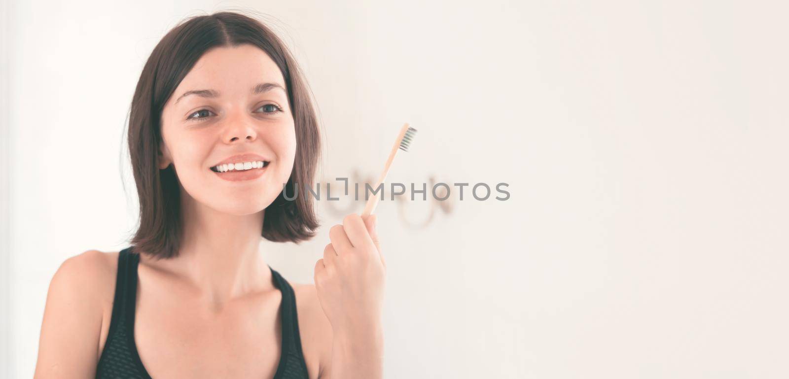 A young smiling girl brushes her teeth with toothpaste in the bathroom by the mirror in the morning, a woman takes good care of the health of tooth enamel and gums.