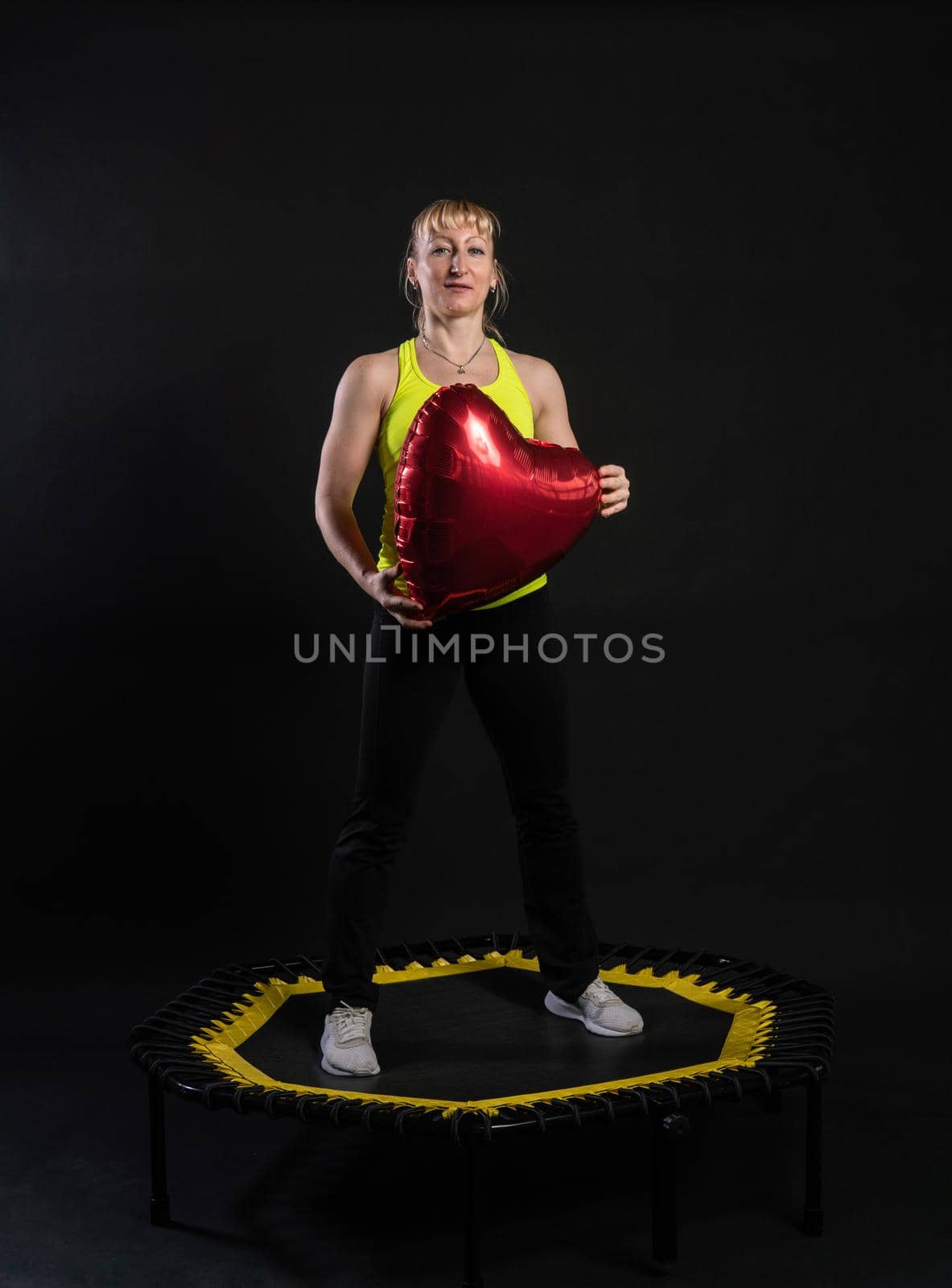 Girl on a fitness trampoline on a black background in a yellow t-shirt trampoline energy active training healthy cardio, weight club. Wellness white sportswear muscle instructor enjoy