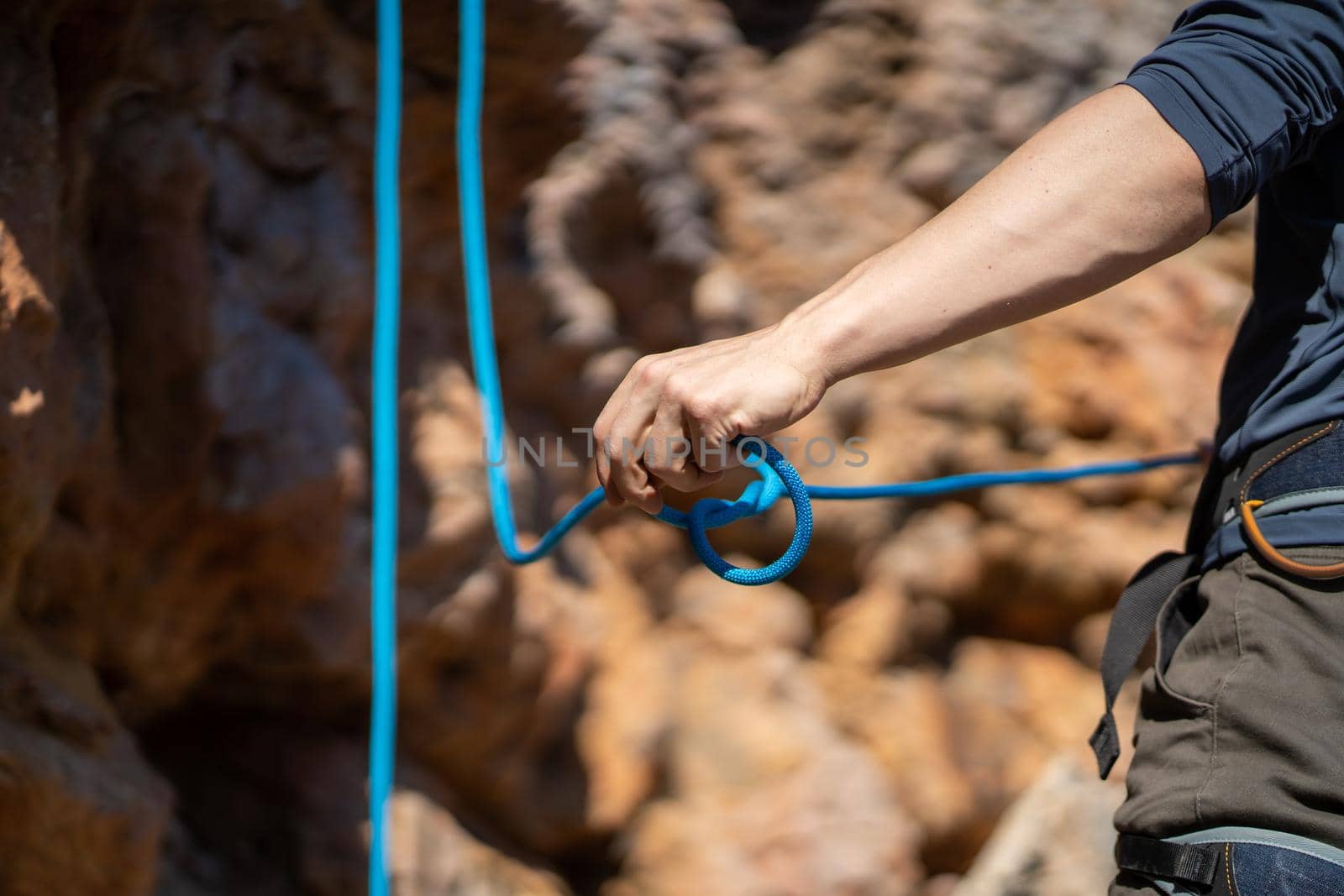 A young man prepares for rock climbing in the mountains outdoor, an athlete ties a figure eight loop on a rope during training, mountaineering on a sunny day, close-up view.
