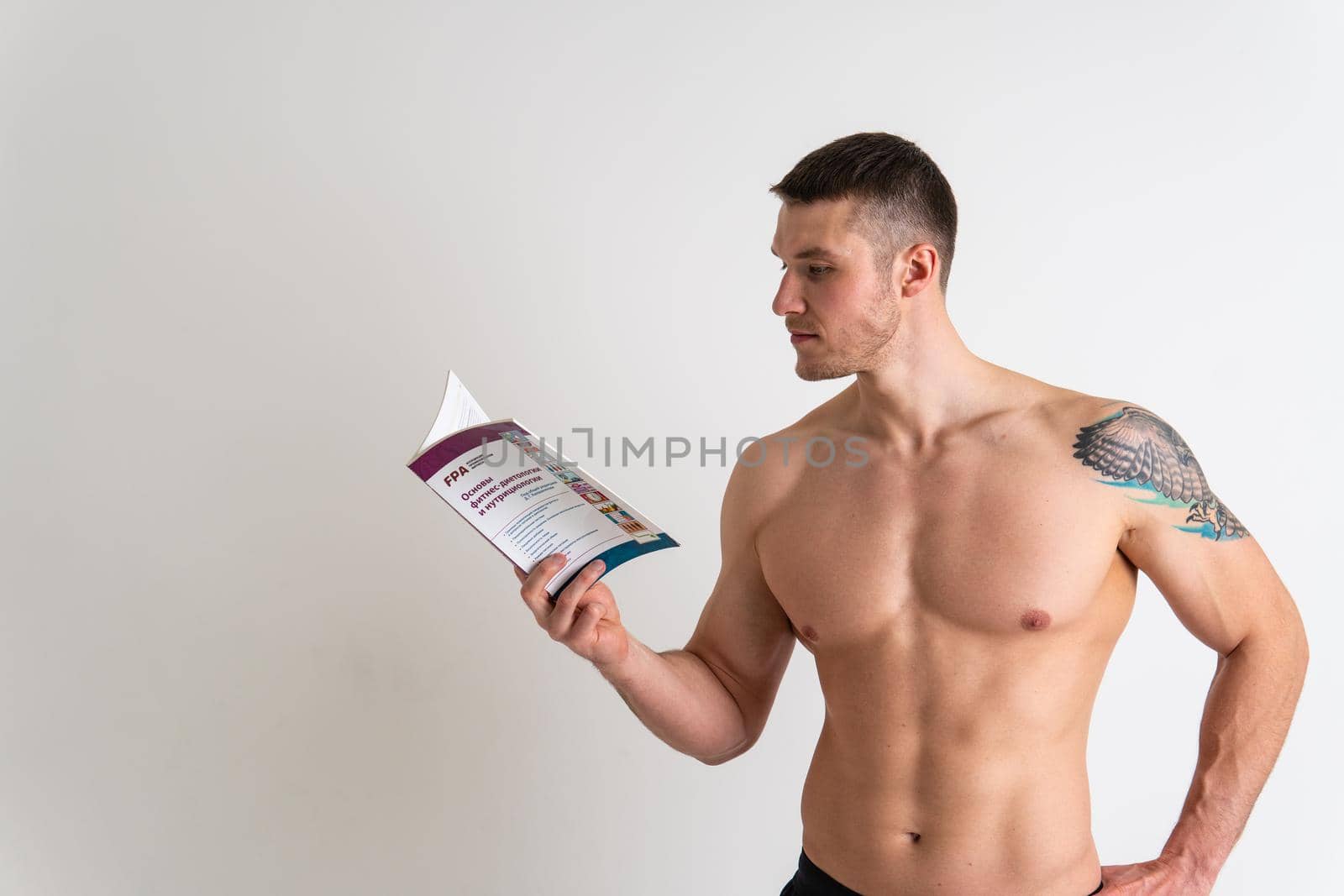 Bodybuilder reads the book on a white background isolated at the bottom of his head on his hands bodybuilder muscular, muscle fitness muscles, sexy sport. Health ABS holding, beach tan