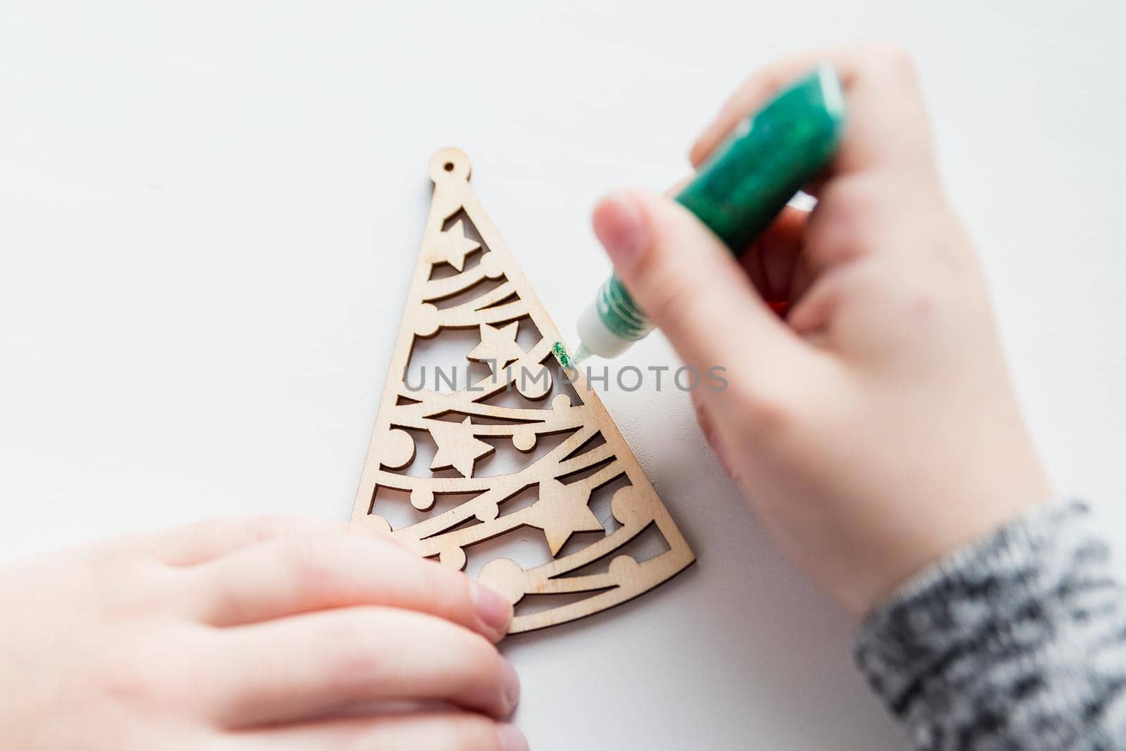 Little child painting wooden Christmas tree decorations sitting at table at home. Holiday DIY concept for children.