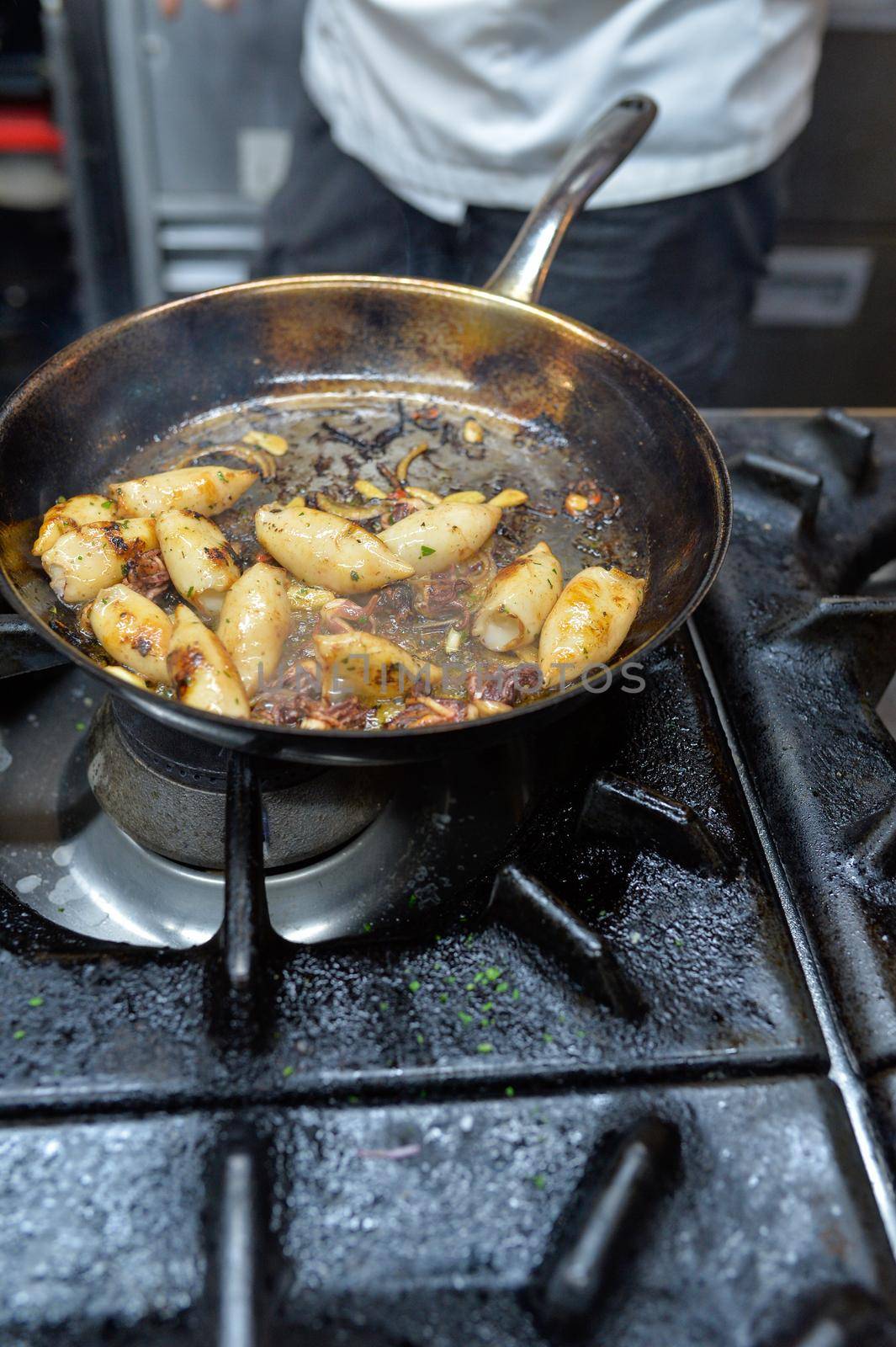 In a restaurant kitchen, calamari are grilled by the chef on a gas stove.