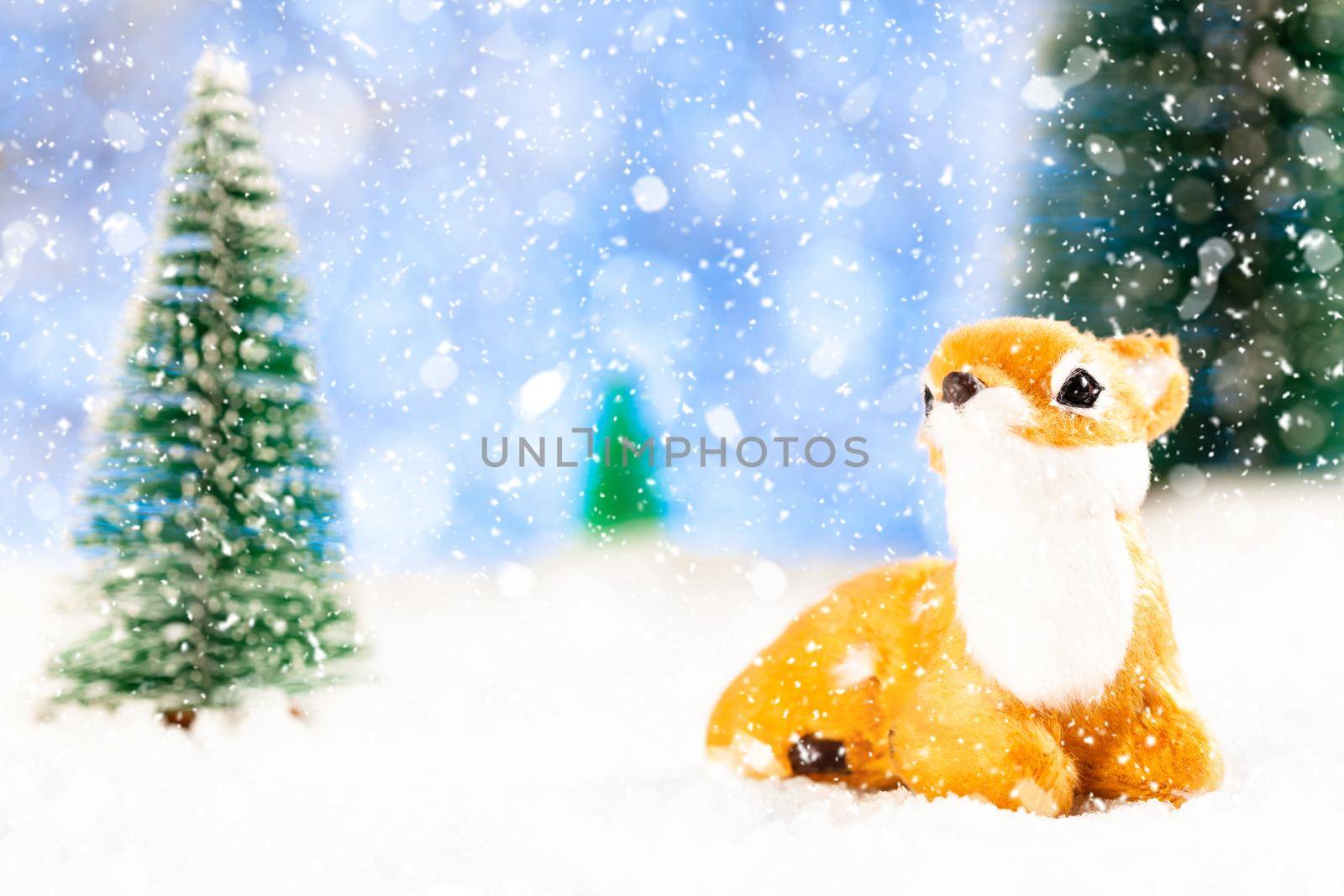 little toy deer sits in the snow. Around toy fir trees. New year greeting card.