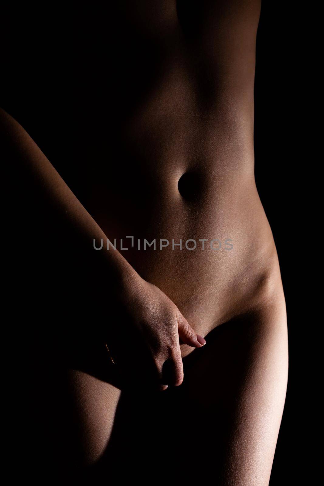female naked slim belly and pussy covered with hand on black background. Soft focus. Non-Explicit Nudity
