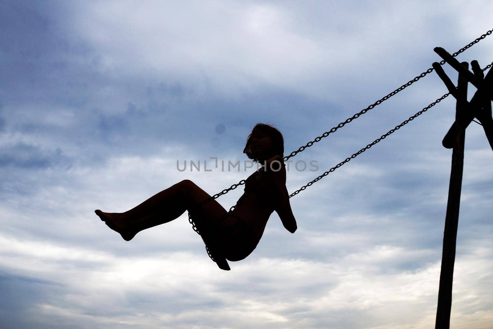 girl swinging on a swing, silhouette against a cloudy sky by Annado