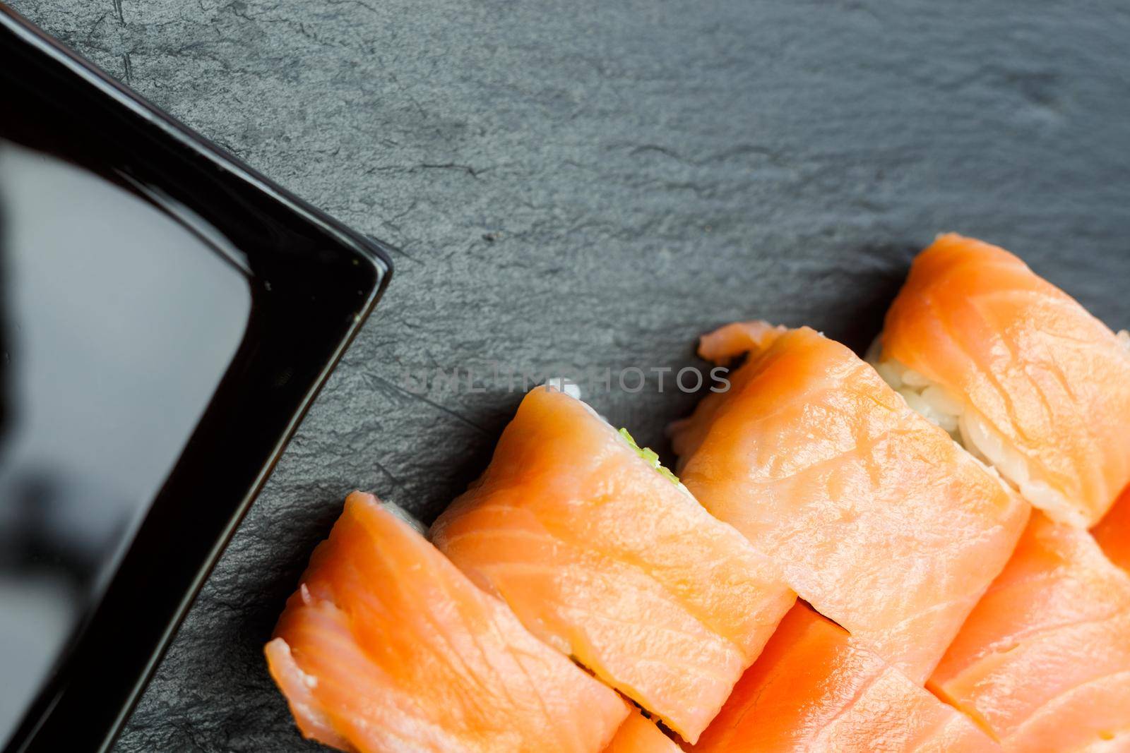 Salmon sushi rolls on a black stone plate.