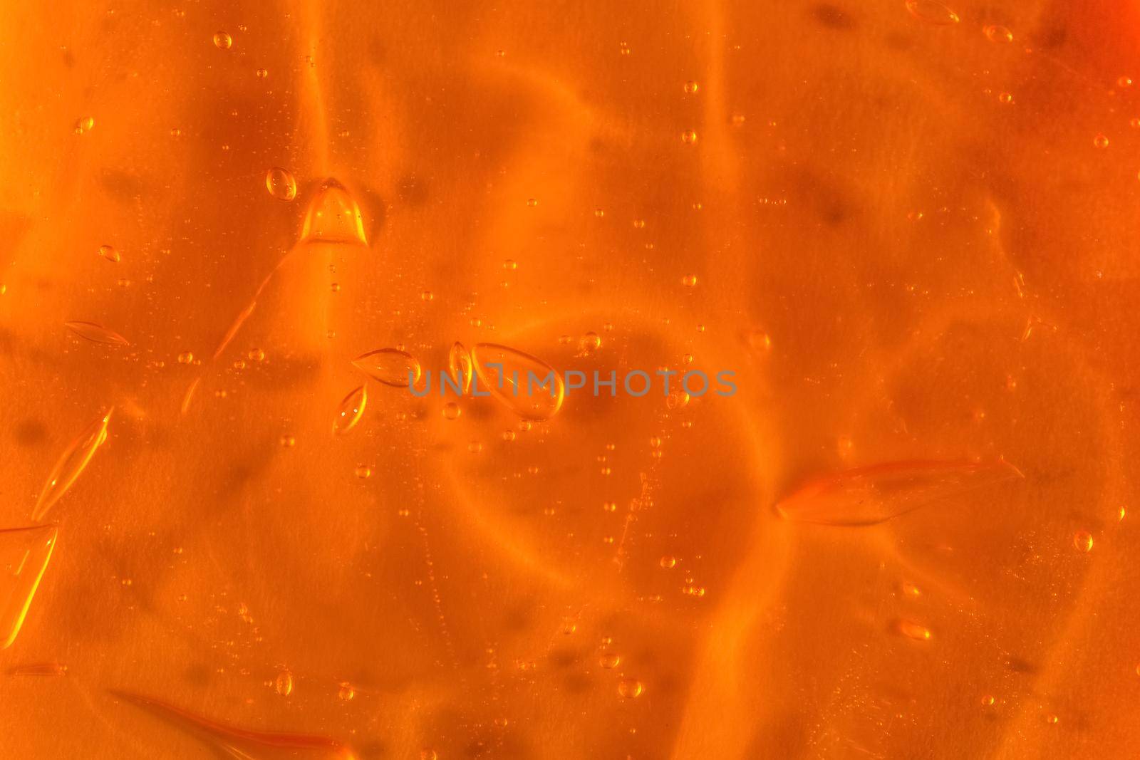 Texture of transparent yellow gel with air bubbles and waves on orange background. Concept of skin moisturizing, body care and prevention of covid19. Liquid beauty product closeup. Backdrop, flat lay